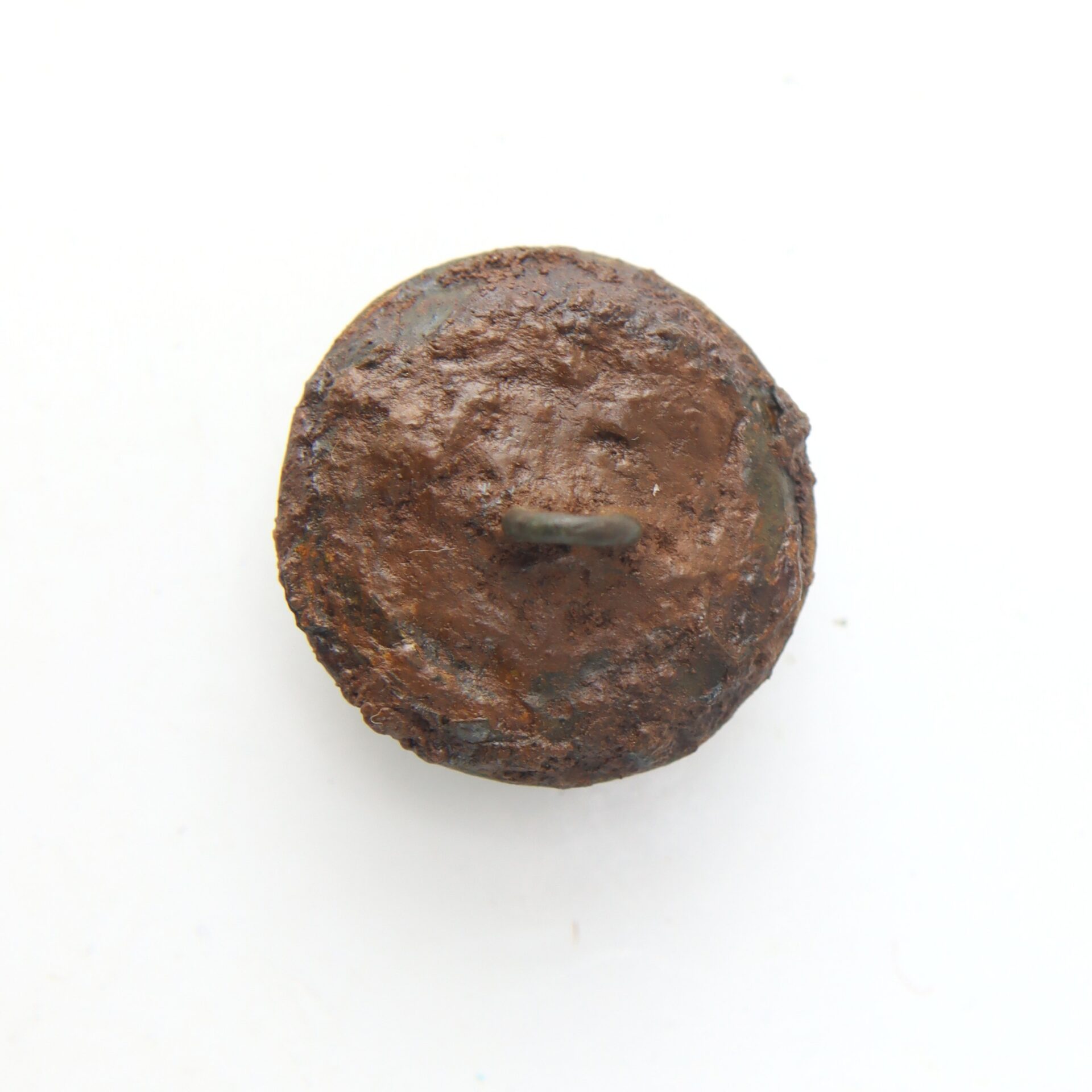 A rusty, round metal button with a shank on the back, photographed on a white background.