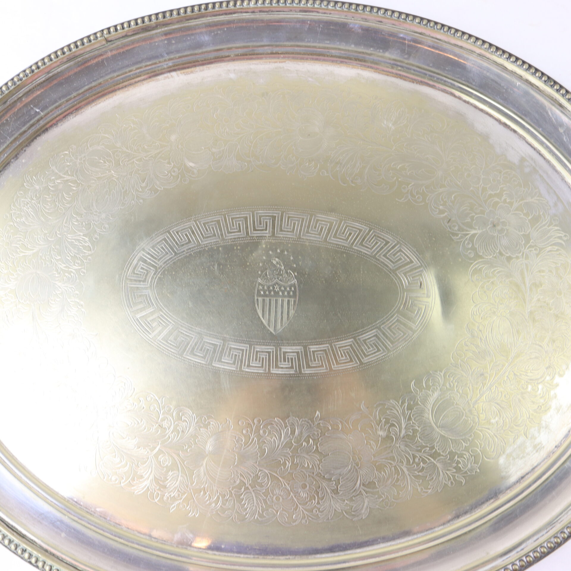 Silver serving tray with ornate floral engravings and a decorative central crest featuring stars and stripes.