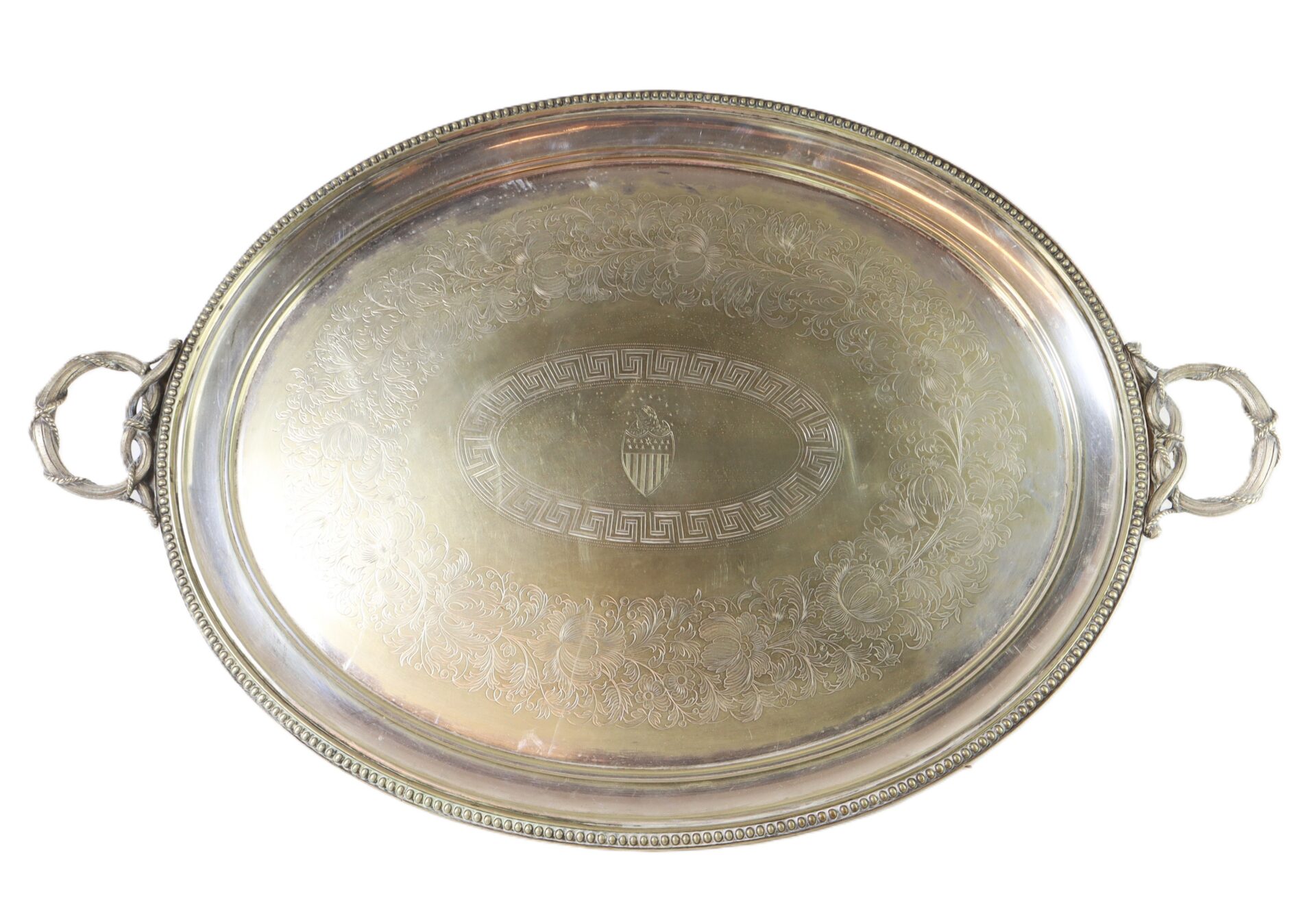 Oval silver serving tray with ornate handles, detailed engraved floral pattern, and a small shield emblem in the center.