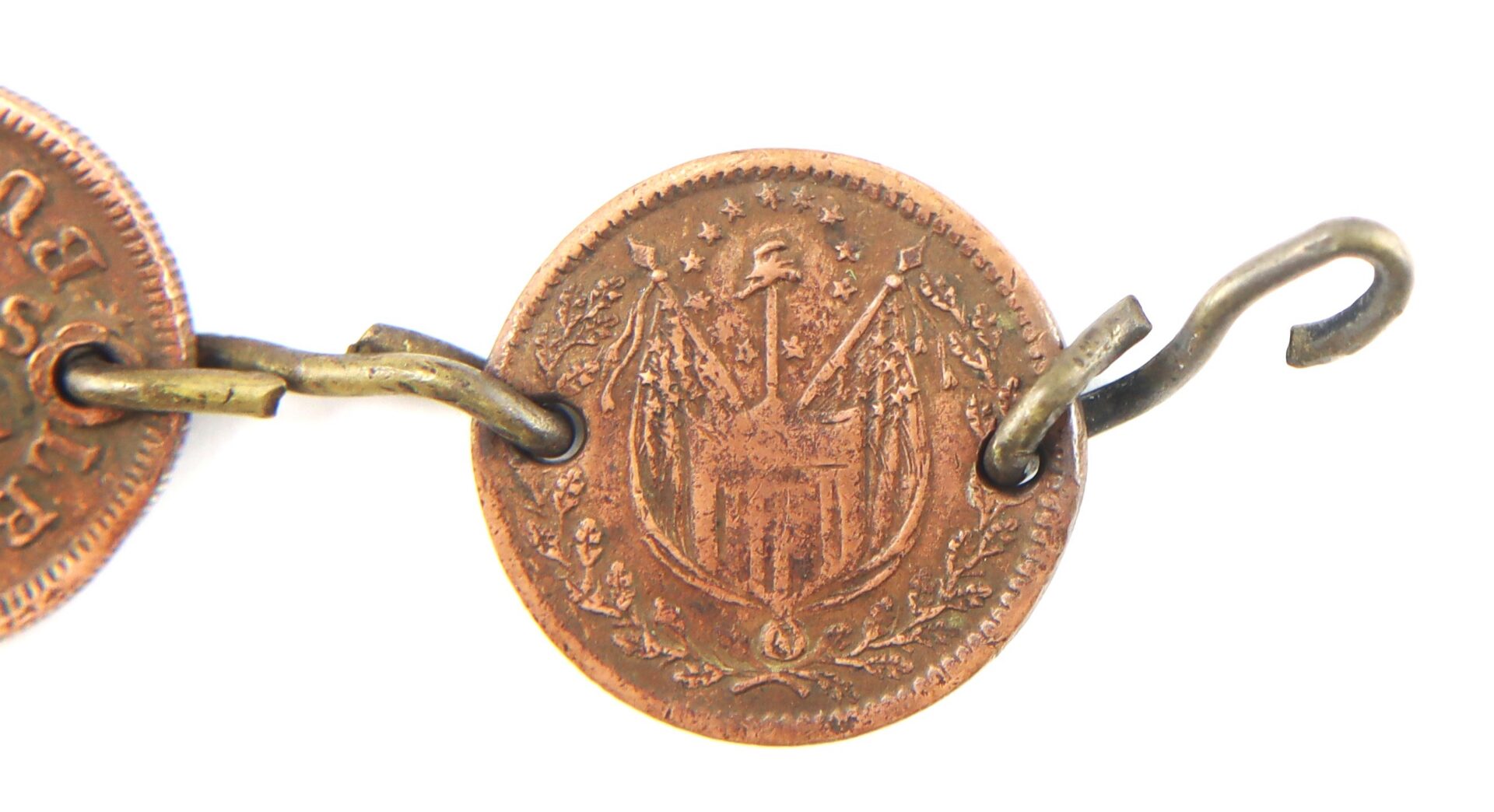 A close-up of a coin with detailed engraving of flags, weapons, and symbols, featuring two metal loops attached on either side.