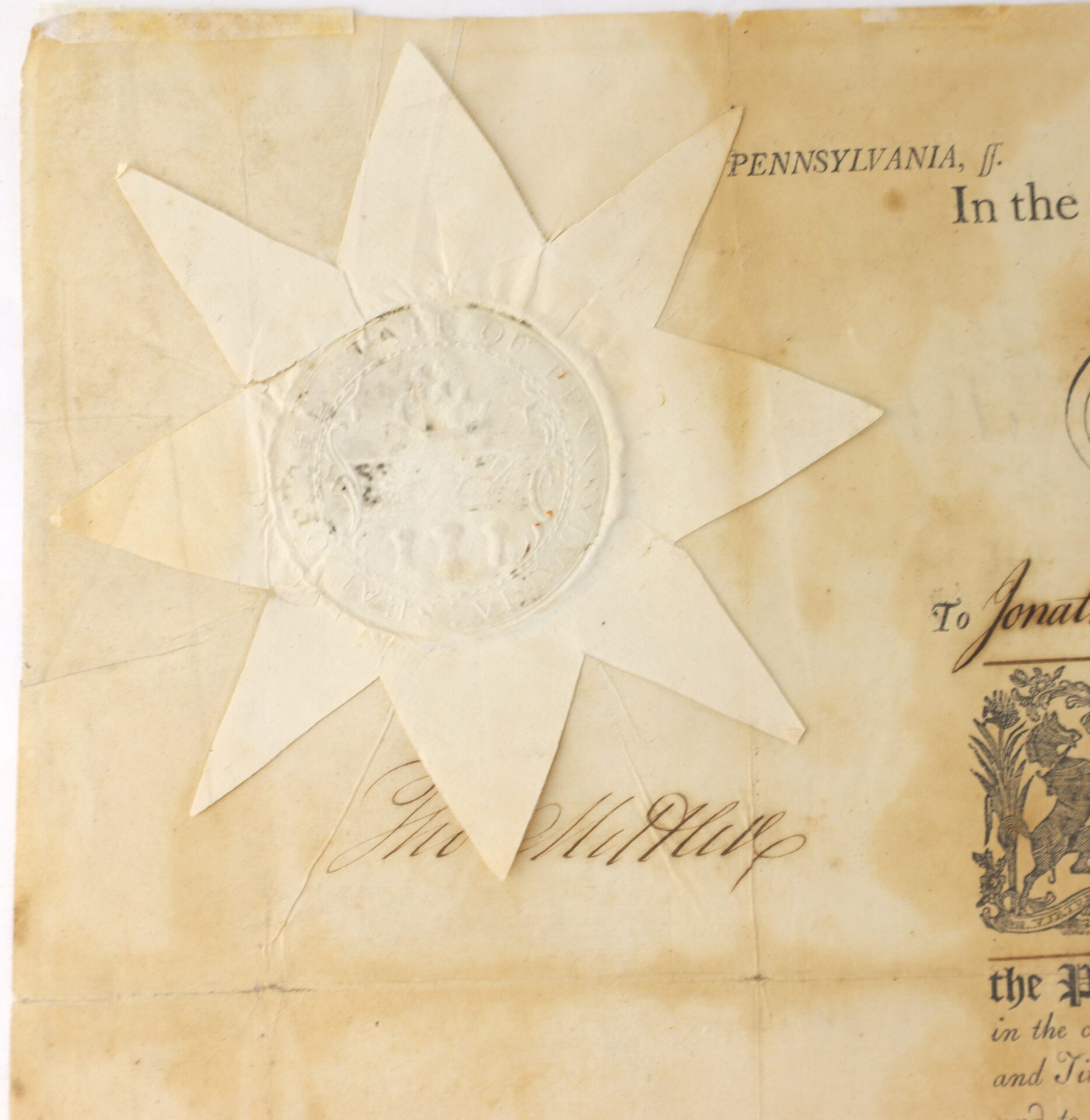 A close-up of an old document features a large, embossed star-shaped seal and a handwritten signature on yellowed paper with visible creases and stains.