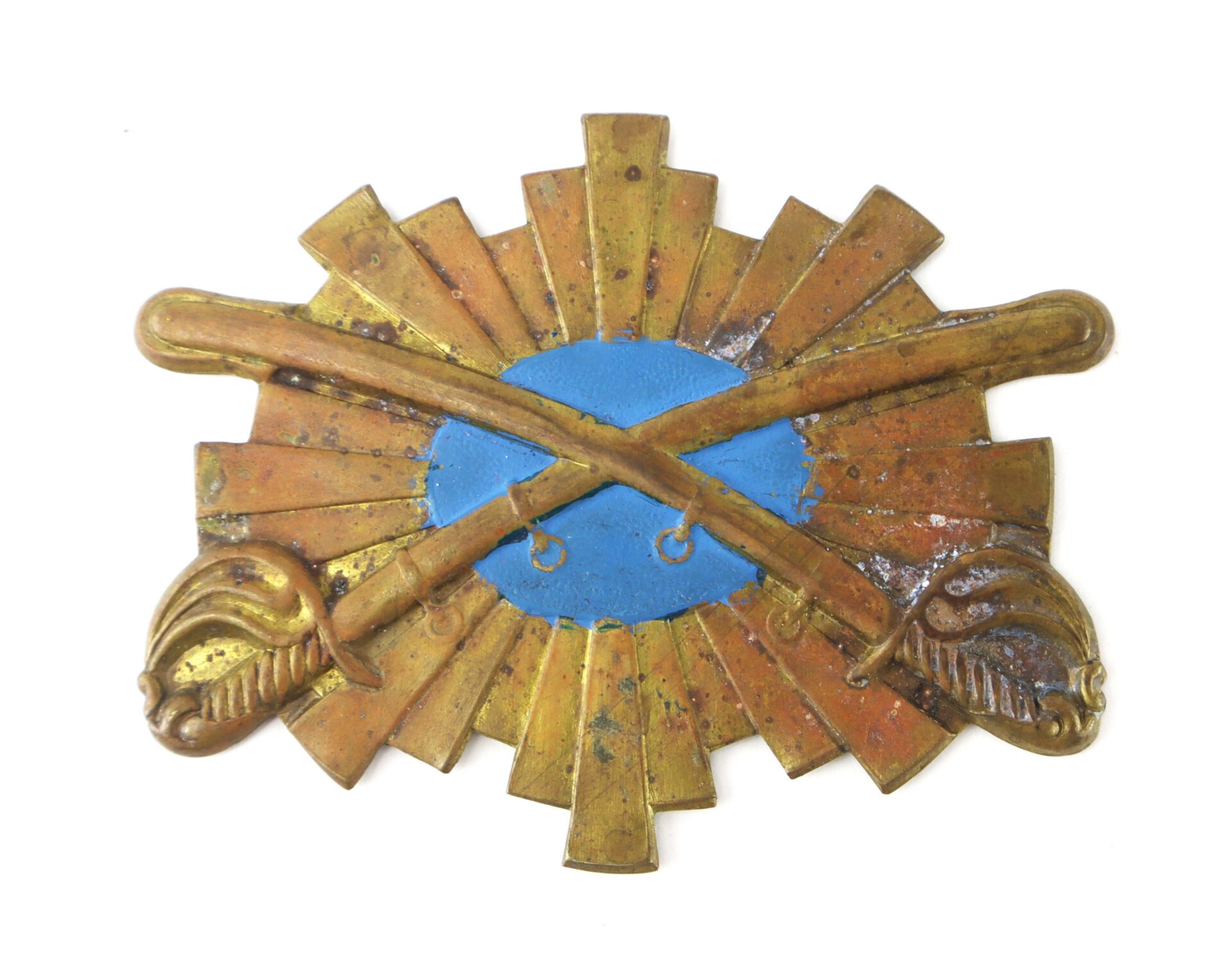A brass military badge with crossed sabers over a blue oval background and a radiating sunburst design.