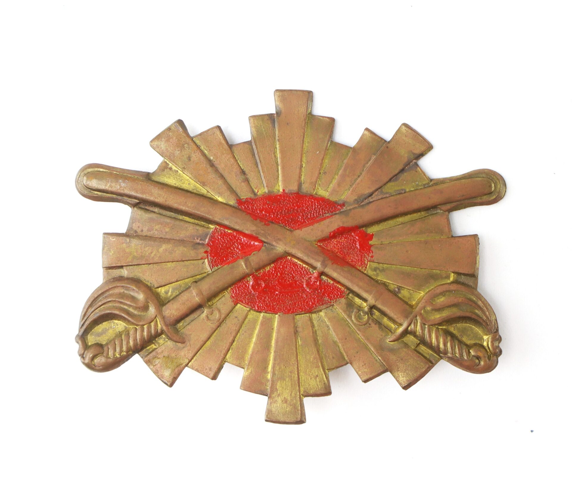 Antique brass military badge with two crossed swords and a red circular center on a sunburst background.