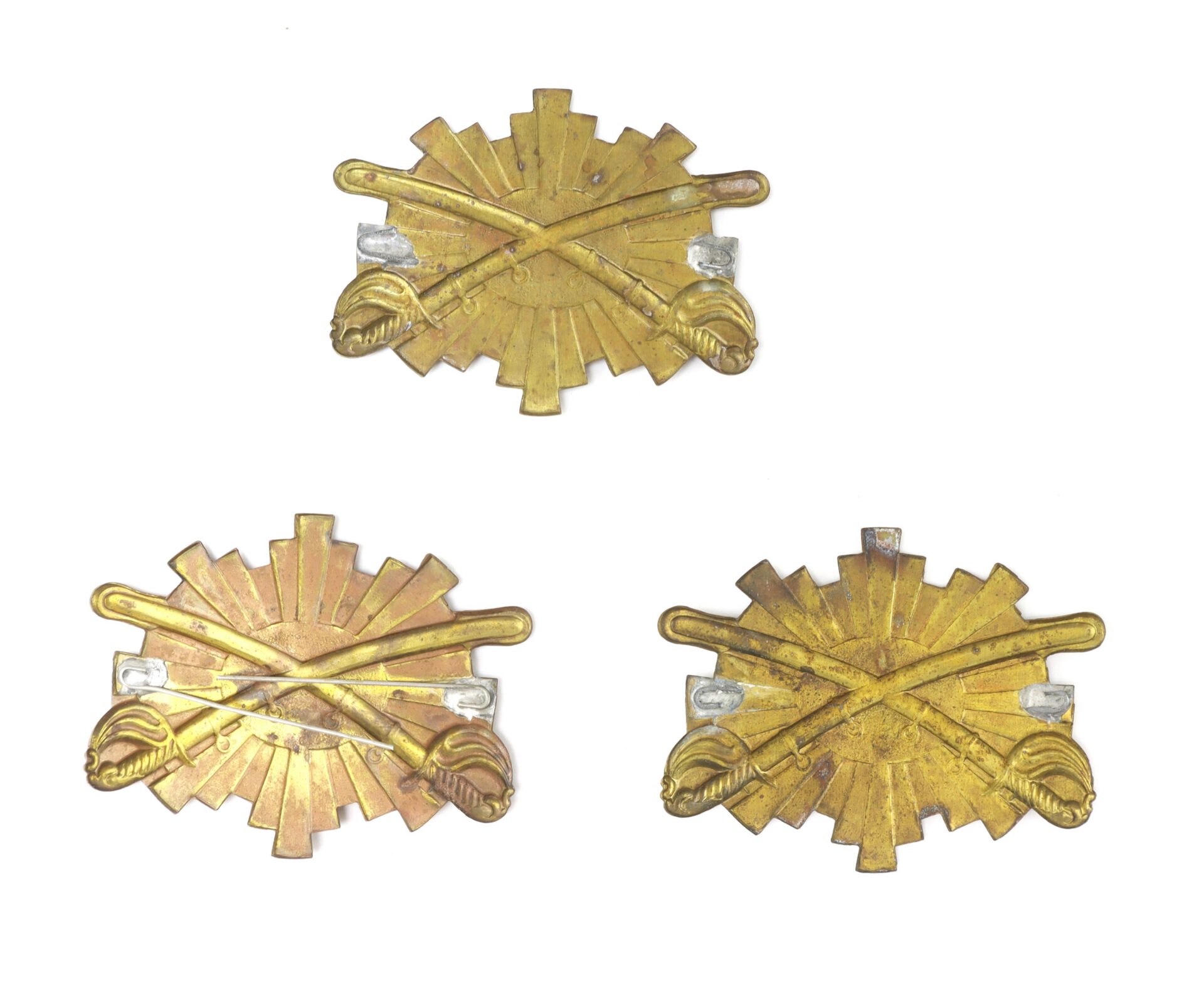 Three brass military insignia pins featuring crossed sabers over a sunburst design, displayed on a white background.