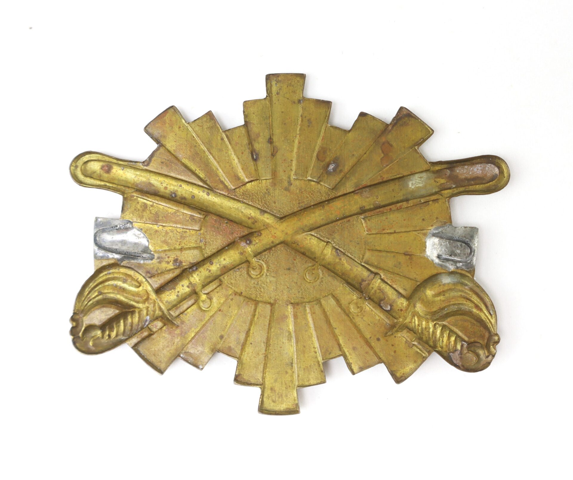 Brass military insignia featuring two crossed sabers in front of a sunburst pattern, with two rectangular metal clips on each side.