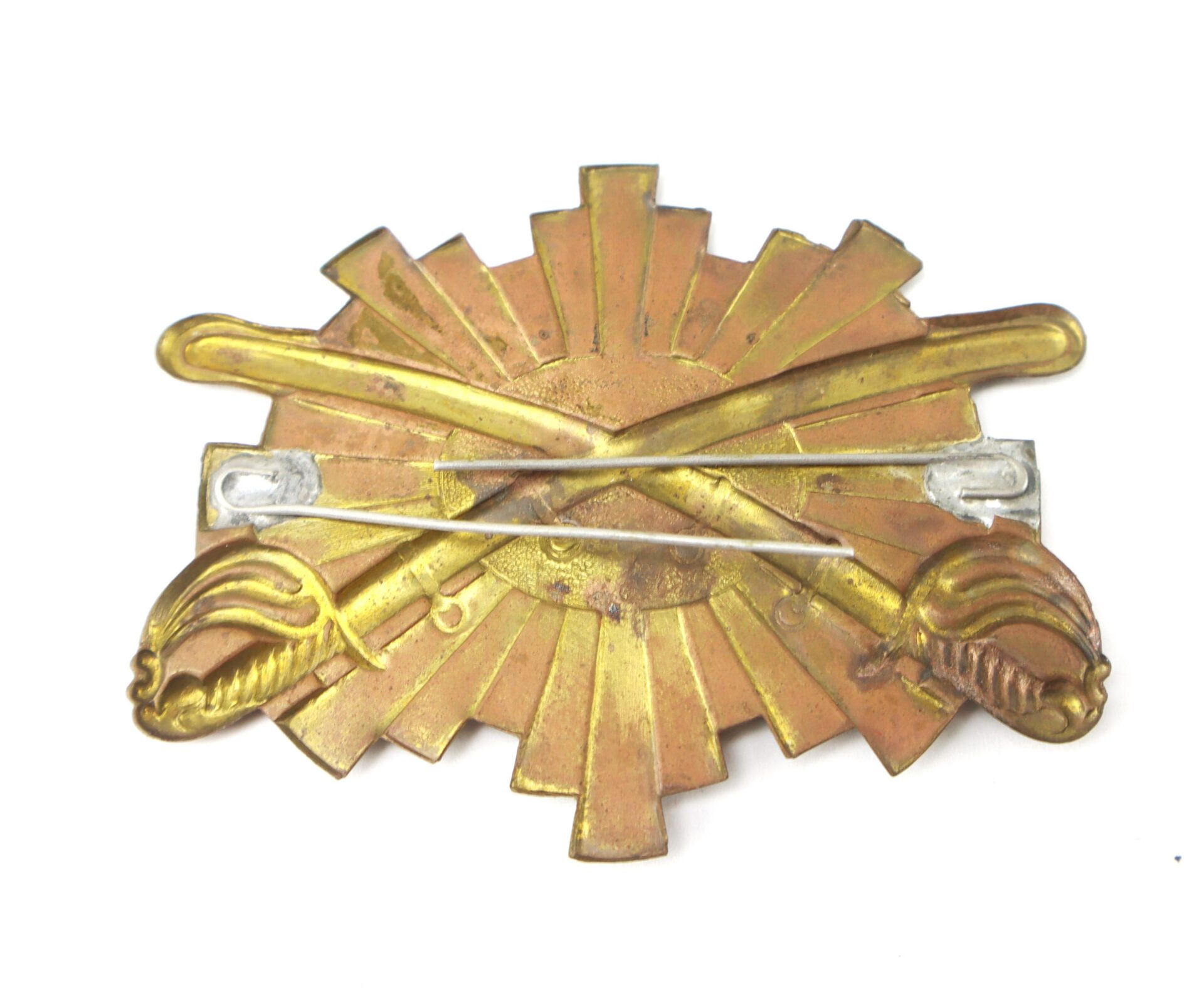 A brass and copper military insignia featuring crossed sabers and a sunburst design.