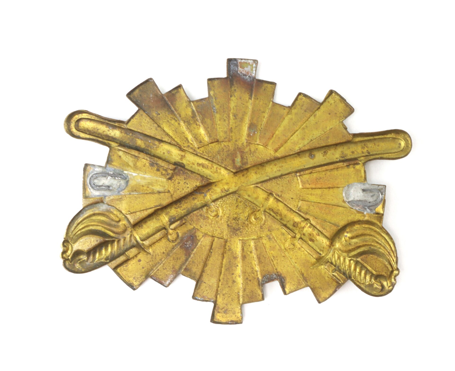 A brass military insignia featuring two crossed swords over a sunburst pattern.