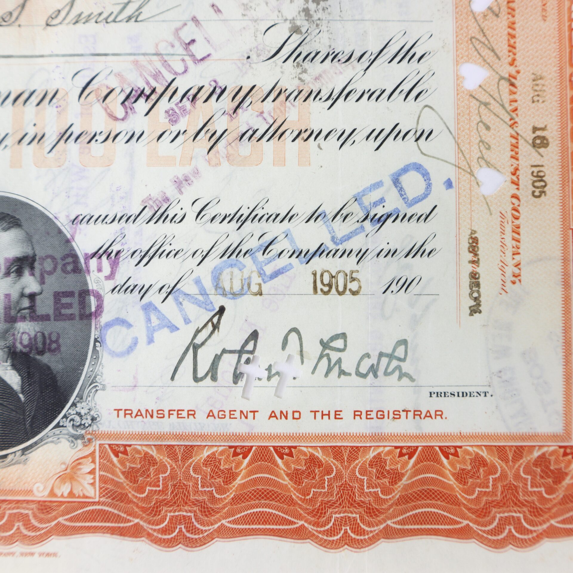 Close-up of a vintage stock certificate with signatures, a visible photo, decorative border, and large blue “CANCELLED” stamp across the center.