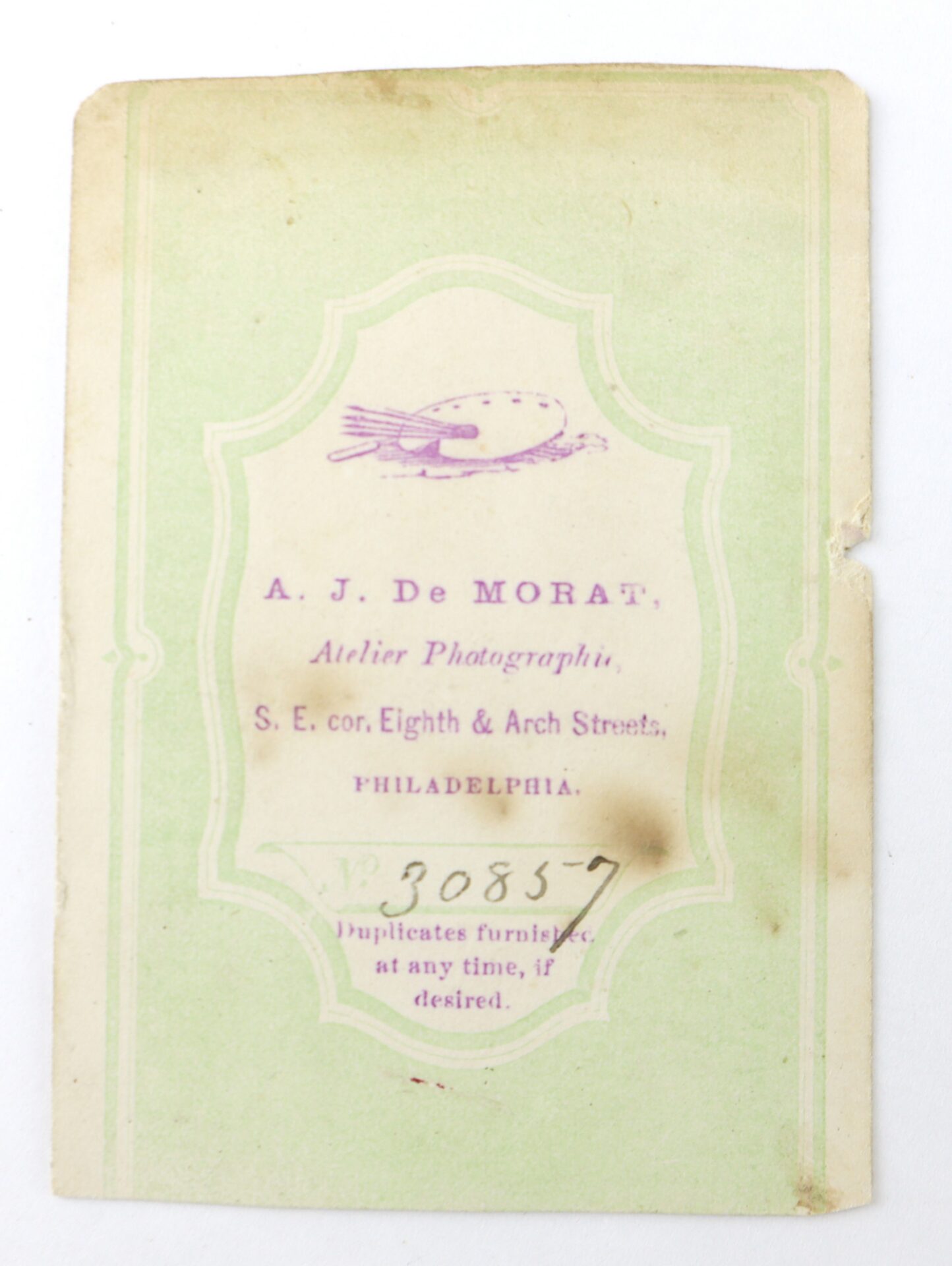 A vintage card with the heading "A. J. De Morat, Atelier Photographique" and an address in Philadelphia, printed in purple text on a pale green background.