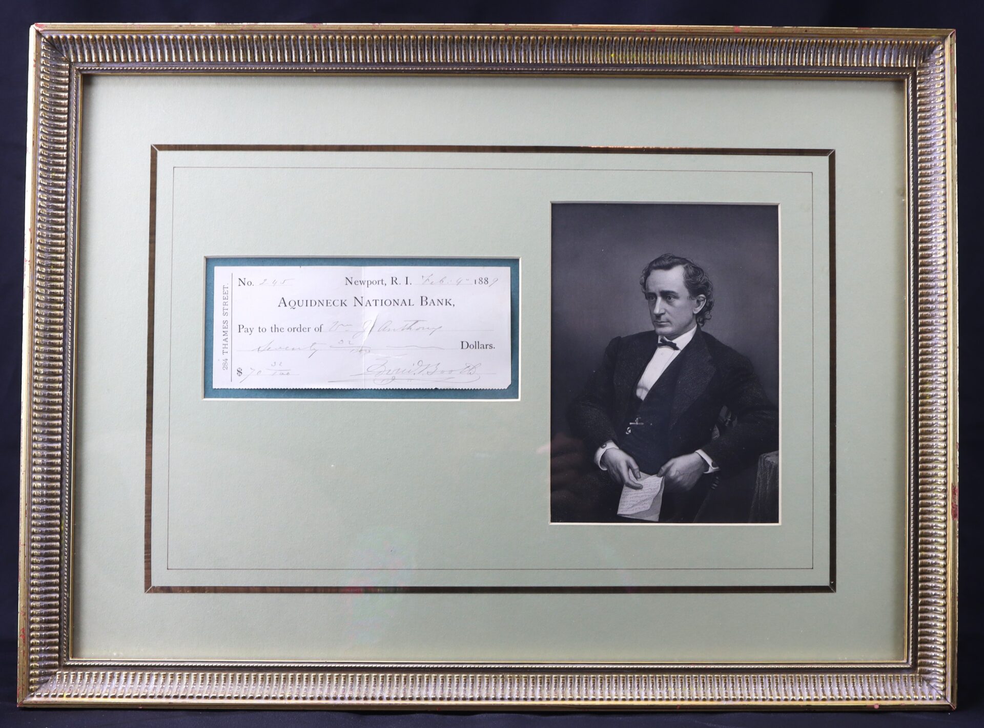 Framed display with an old bank check from Aquidneck National Bank on the left and a black-and-white portrait of a man in formal attire on the right.