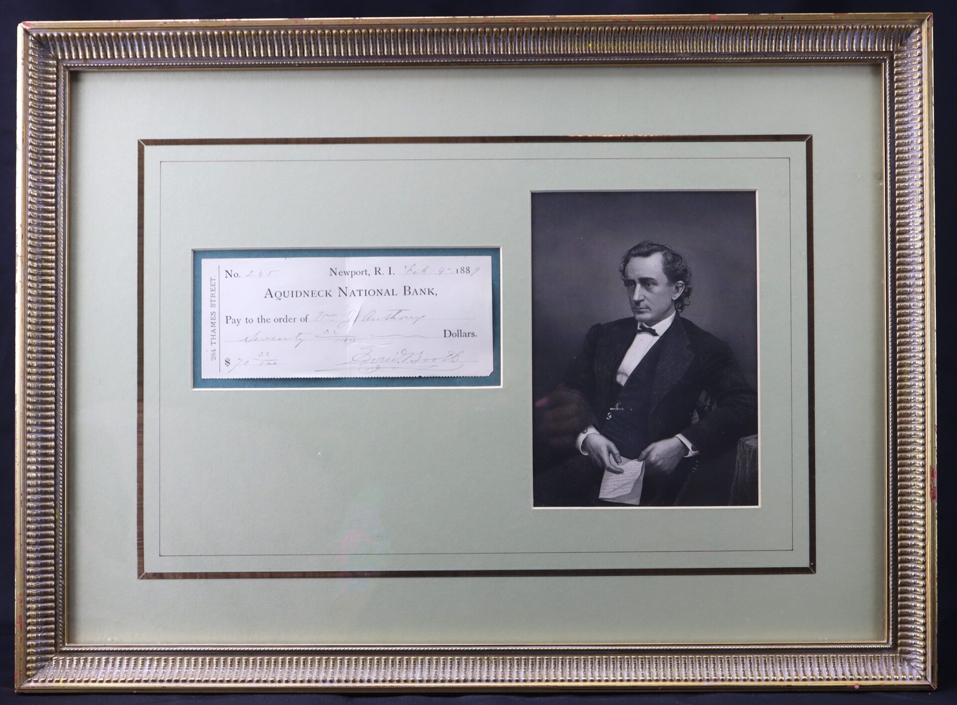 Framed display featuring a historical bank check from Aquidneck National Bank next to a black-and-white portrait of a seated man in formal attire.