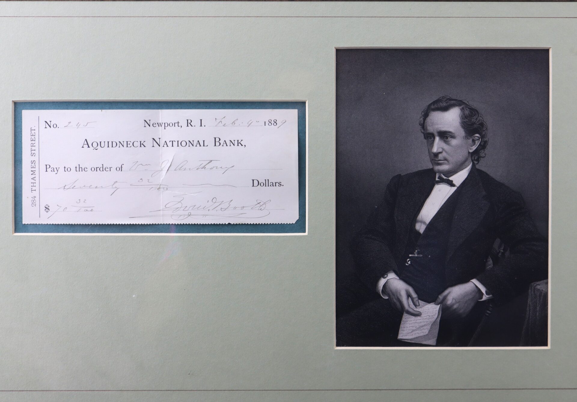 A framed display with a vintage check from Aquidneck National Bank dated 1889 on the left and a black-and-white portrait of a seated man in formal attire on the right.