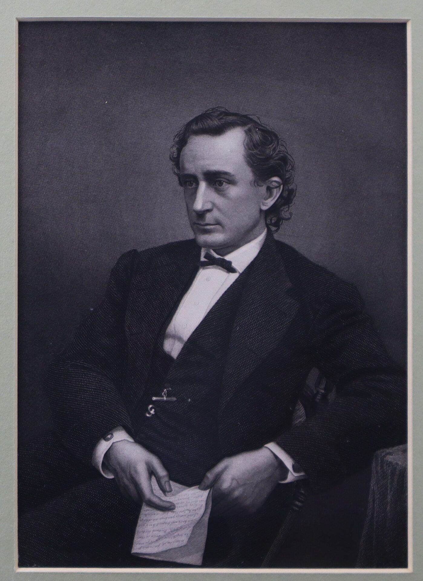 Black and white portrait of a man in formal 19th-century attire, seated and holding a piece of paper, looking slightly to his left.