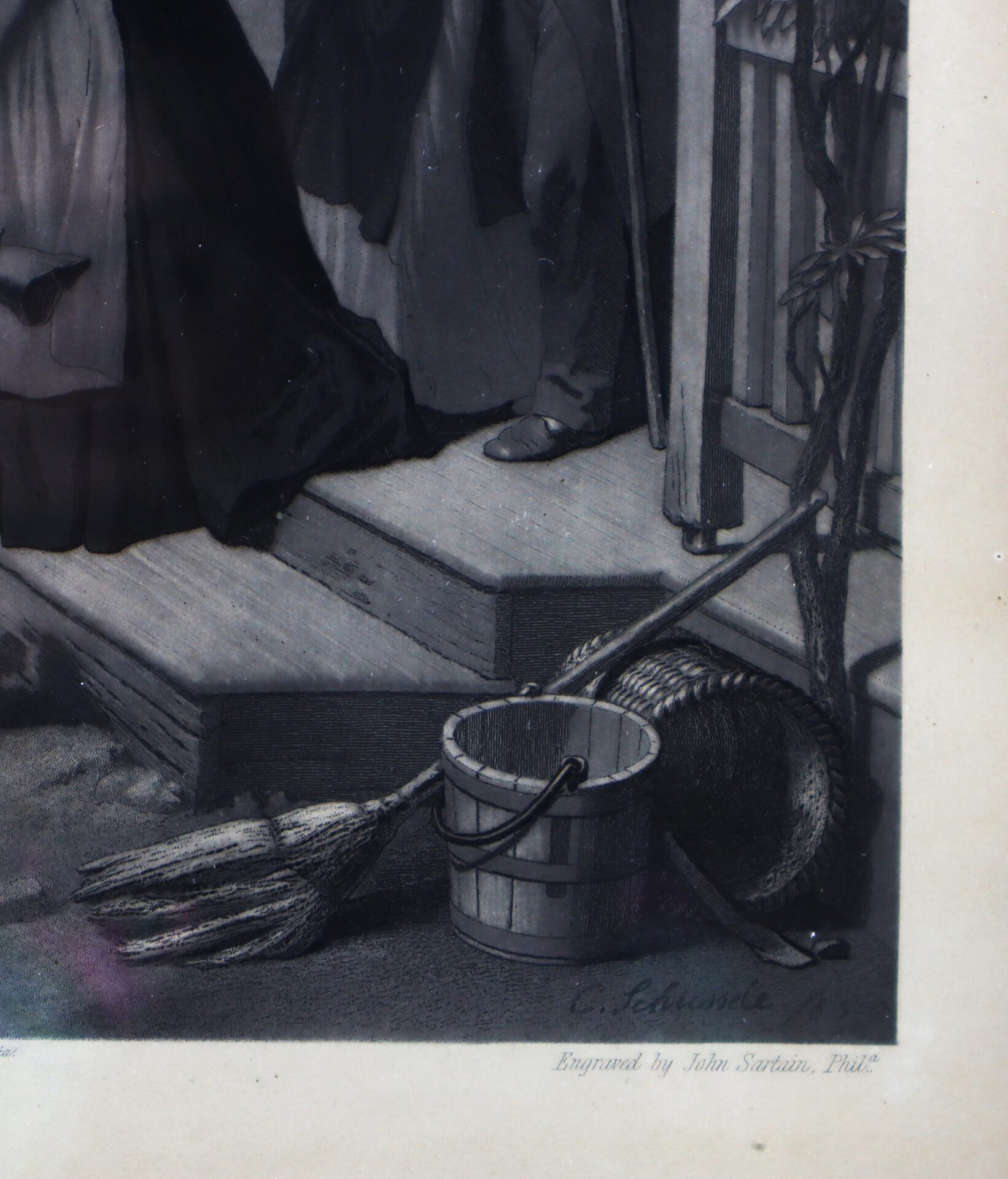 A broom, a wooden bucket, and a straw hat are placed on a wooden step next to a railing, with two people standing nearby.