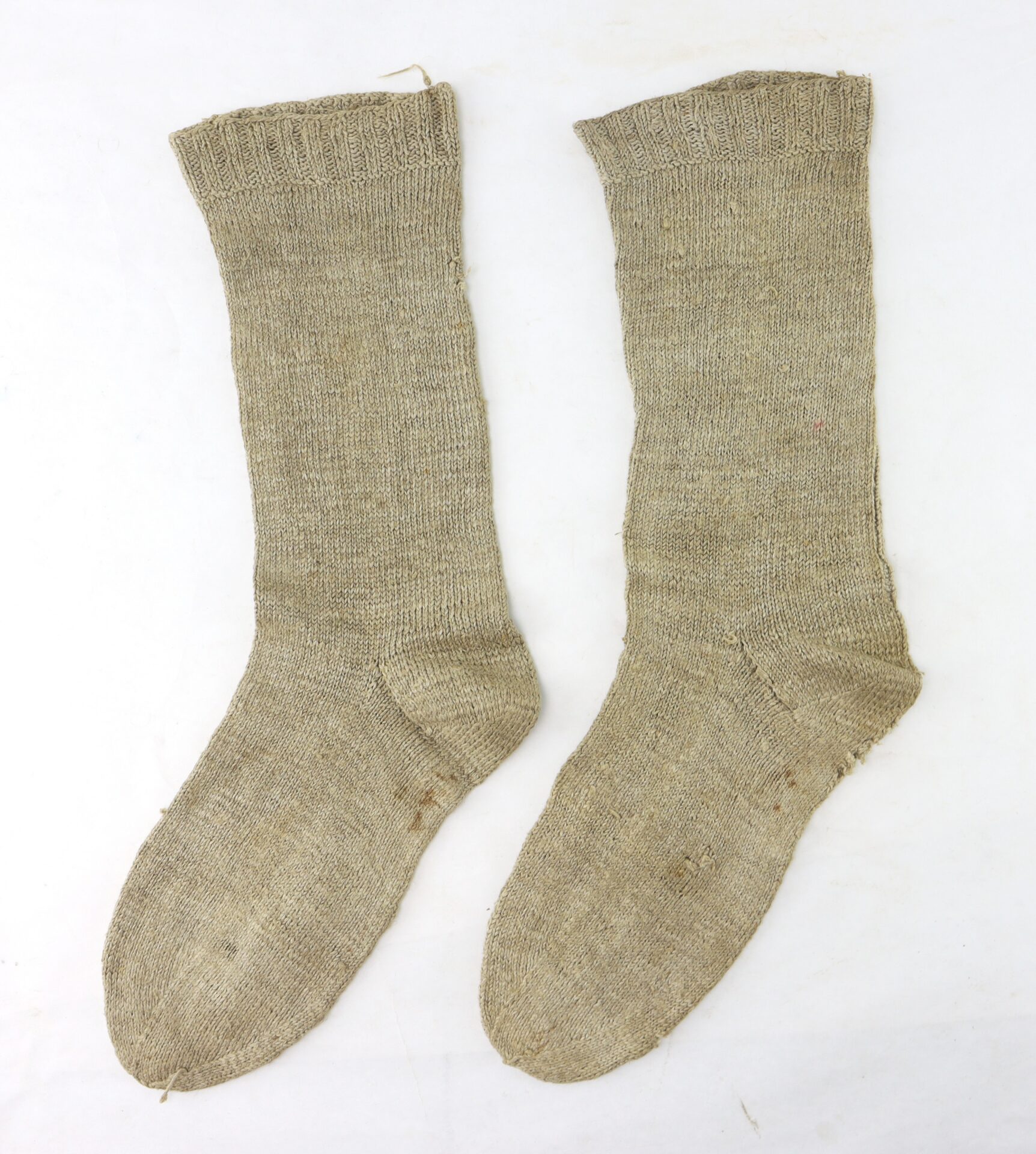 A pair of plain, beige, knitted wool socks laid flat on a white background.