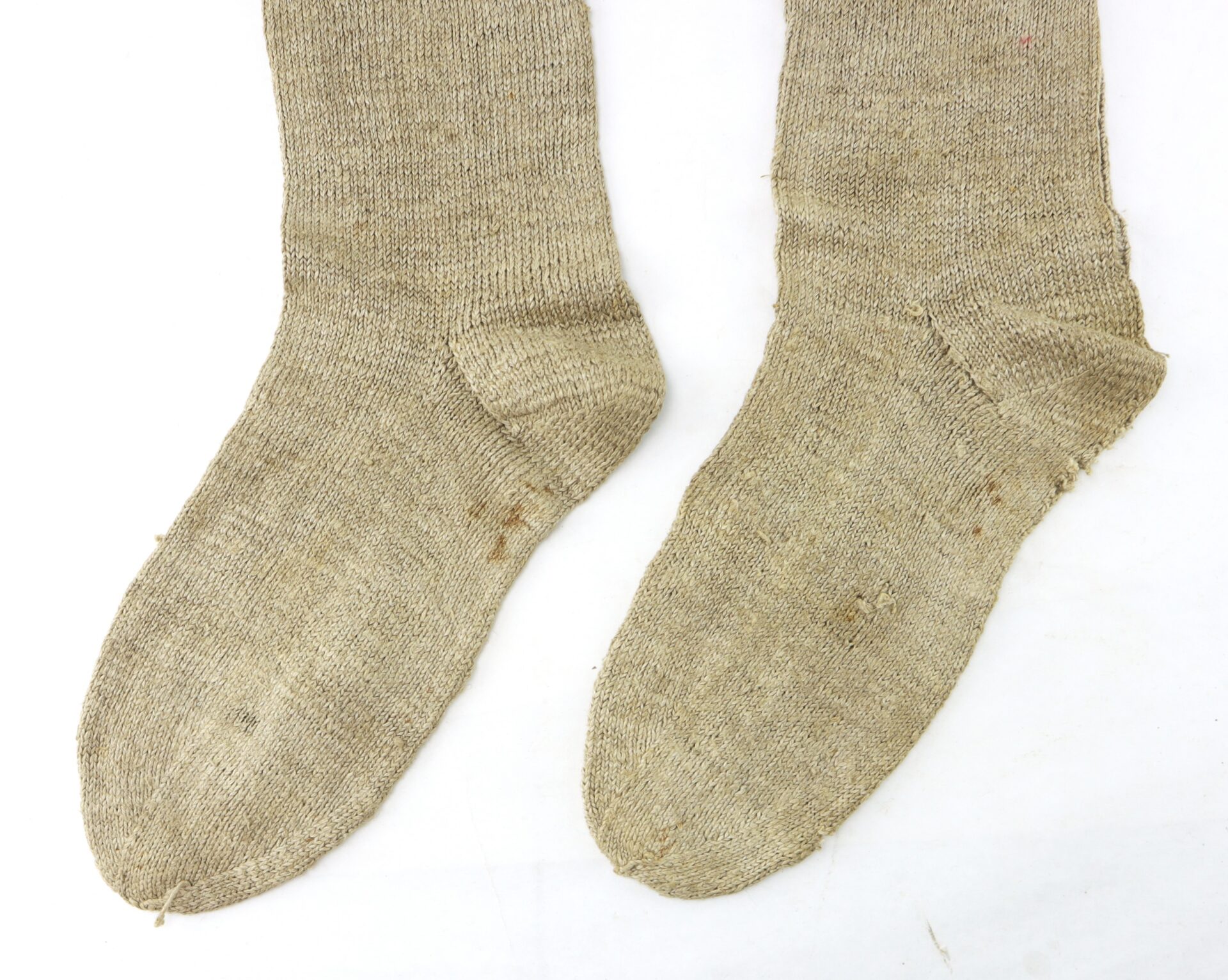 A pair of worn, beige wool socks laid flat on a white surface.