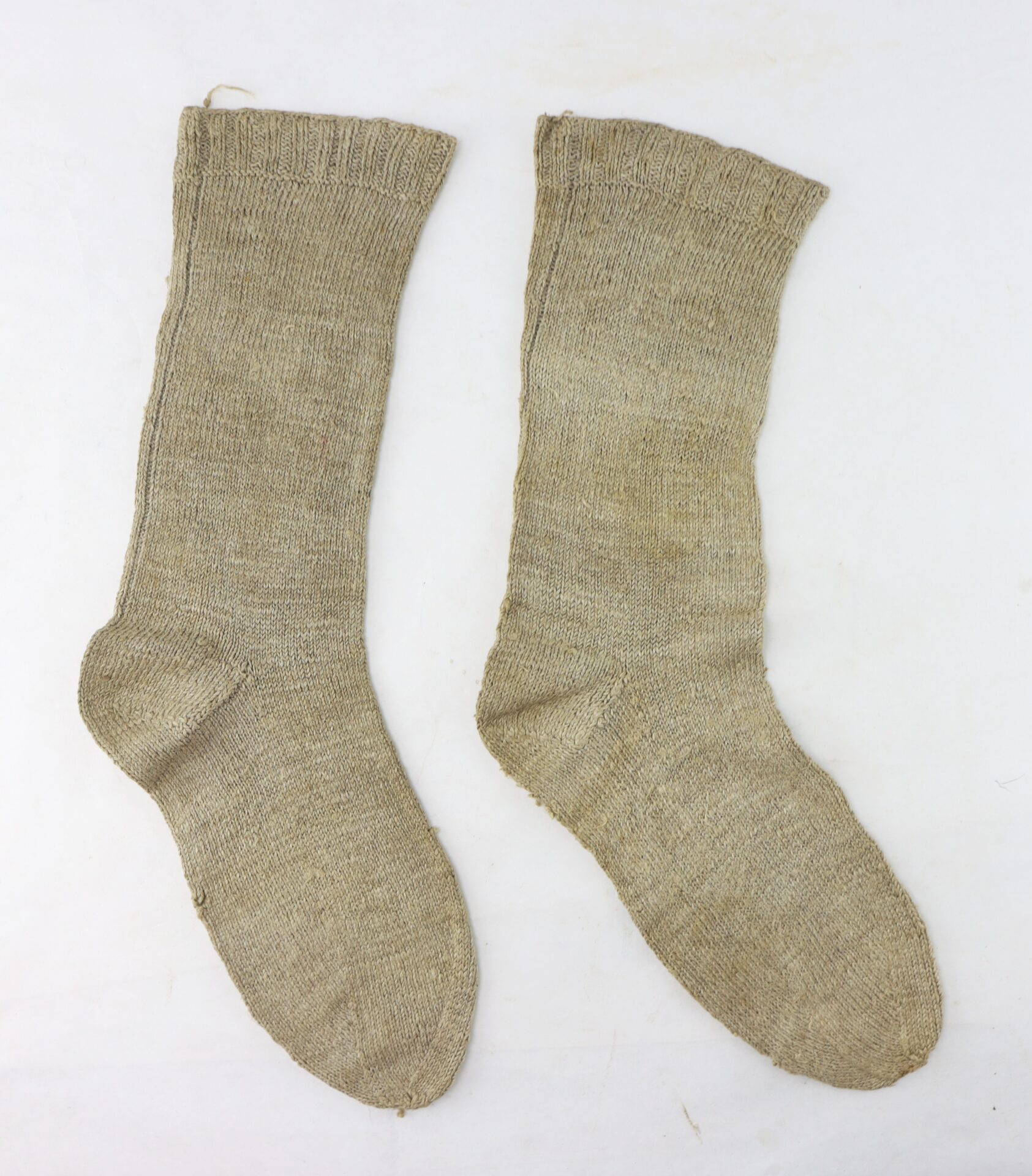 A pair of beige, hand-knitted wool socks laid flat on a white background.