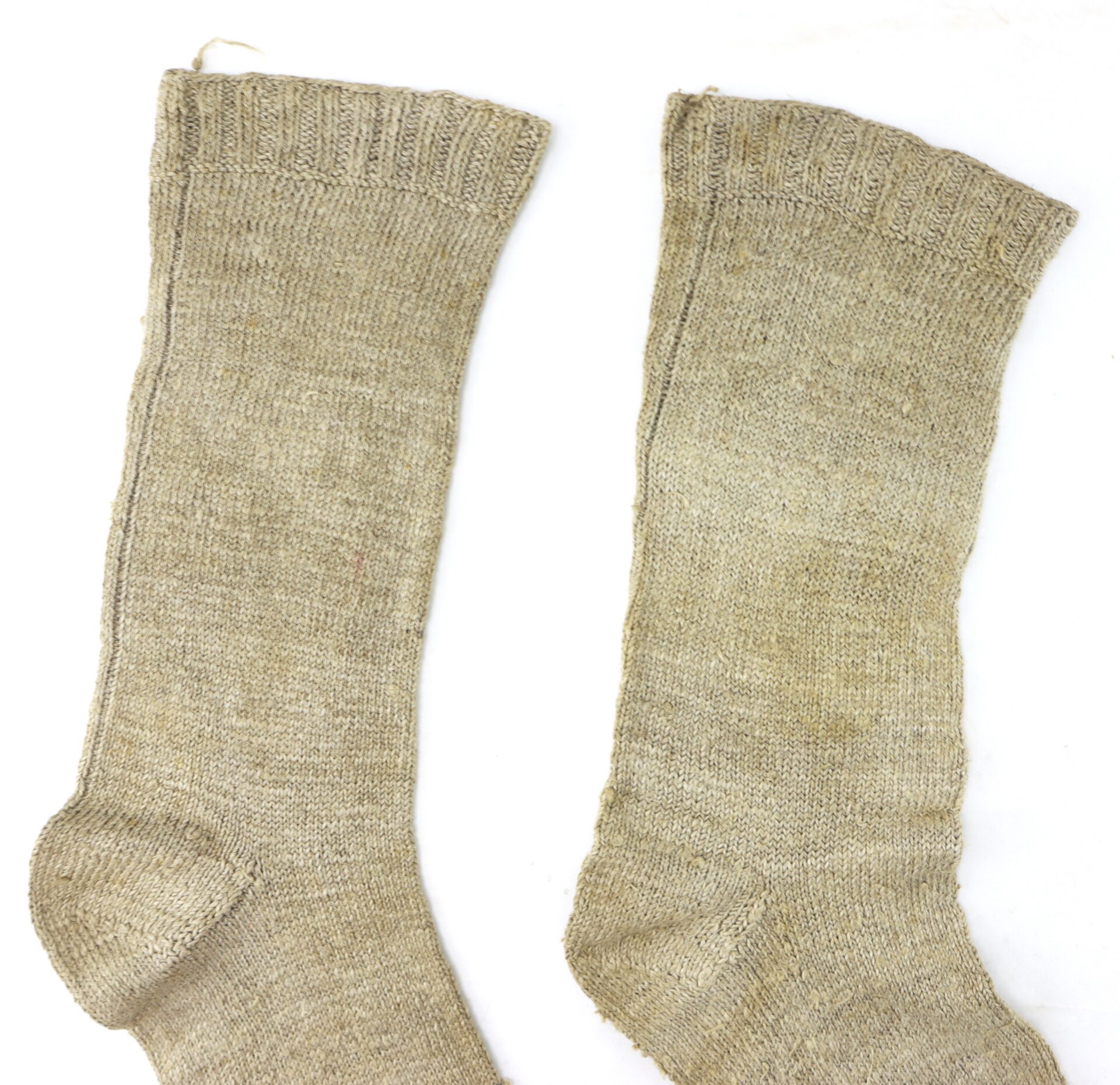 Two beige, woolen knee-high socks are laid flat on a white background, showing signs of wear and uneven texture.
