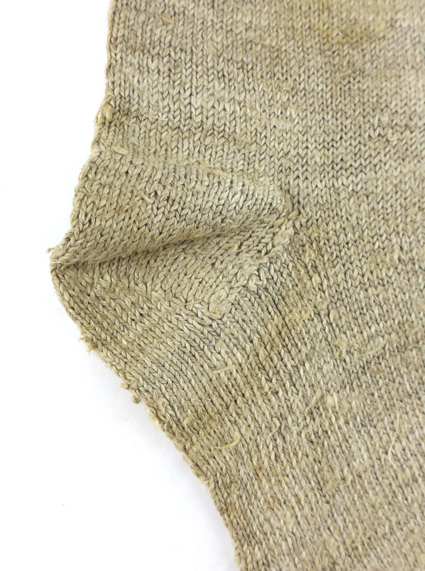 Close-up of a beige knitted fabric with a visible seam and frayed edge against a white background.