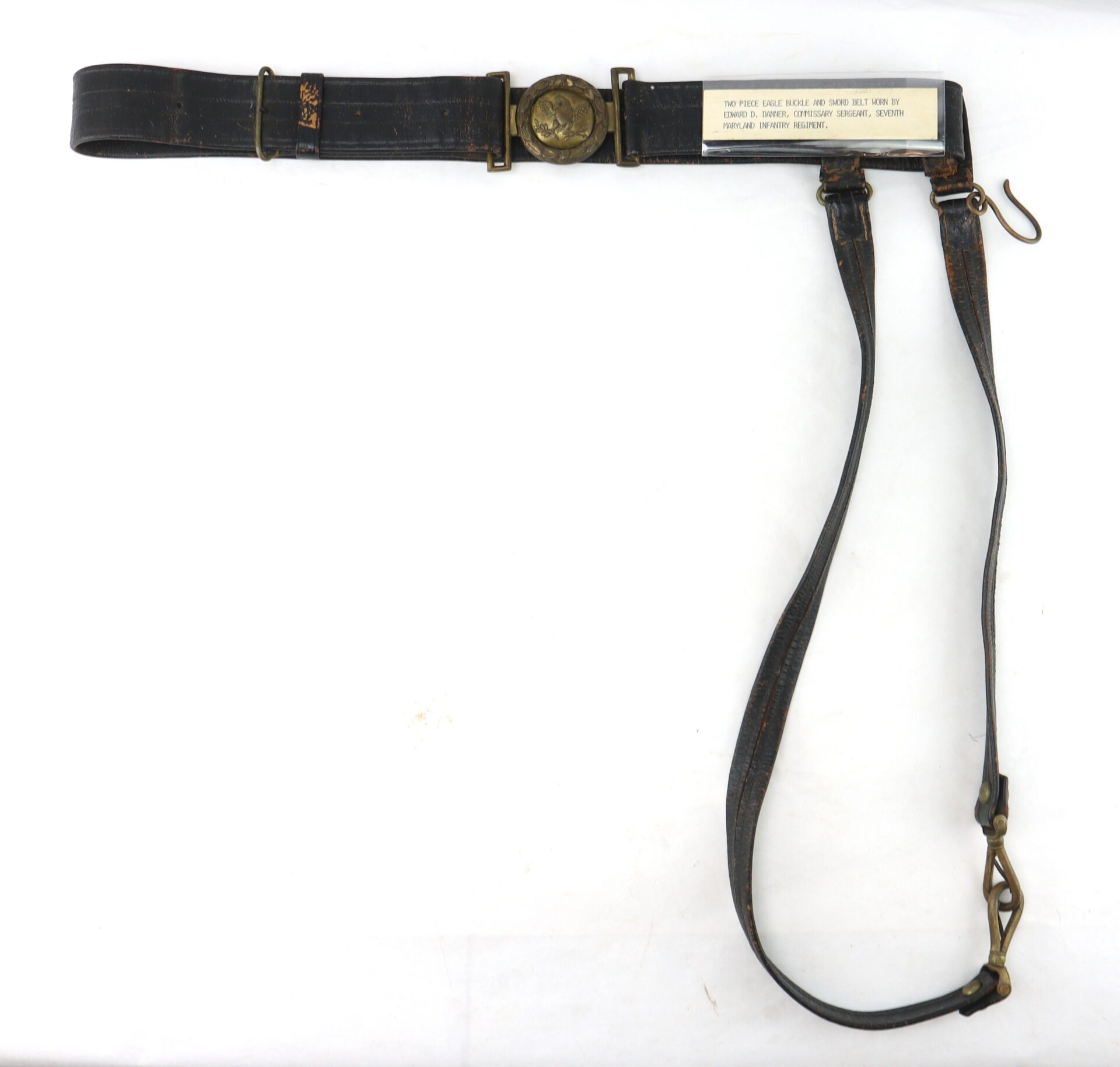 A vintage military leather belt with brass hardware, a central buckle, a shoulder strap, and a tag containing printed instructions.