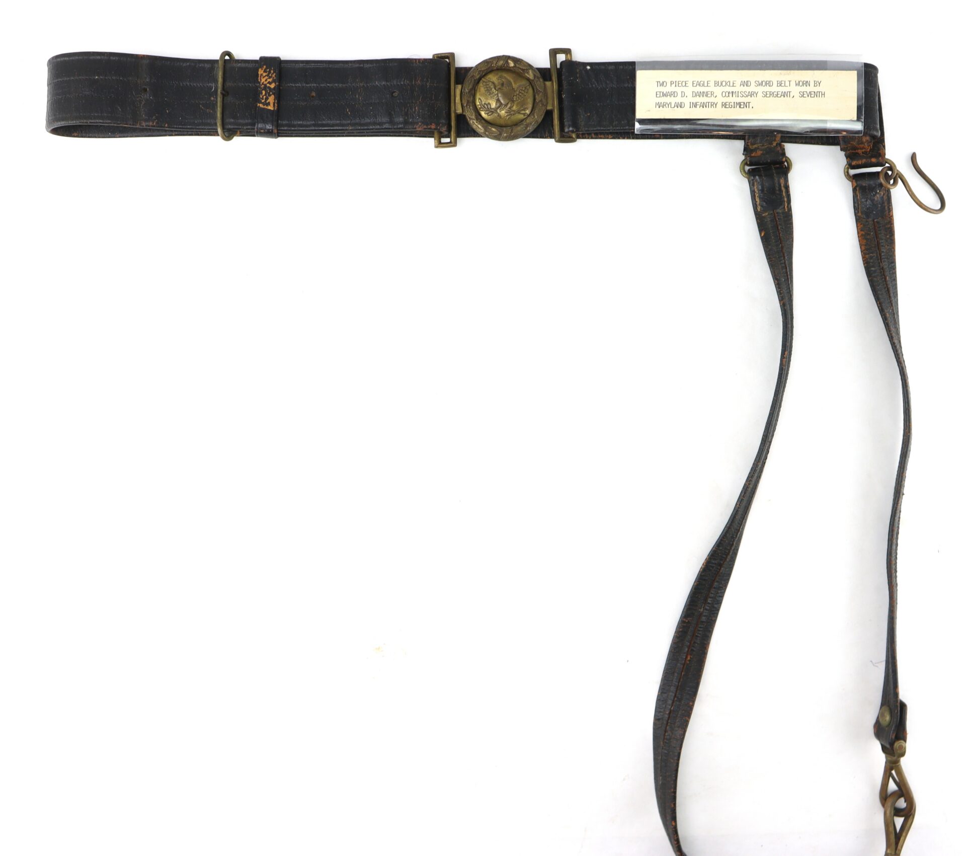 A vintage leather military belt with brass buckle, shoulder strap attachments, and a white label detailing the award and recipients.