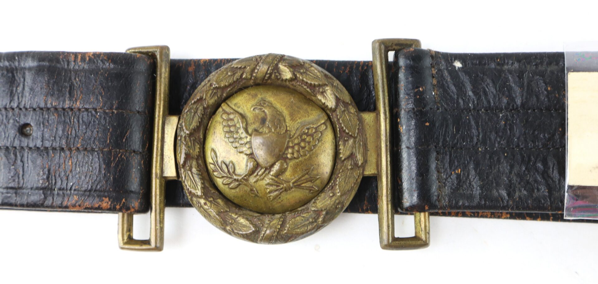 A worn black leather belt with a brass buckle featuring an eagle emblem inside a wreath.