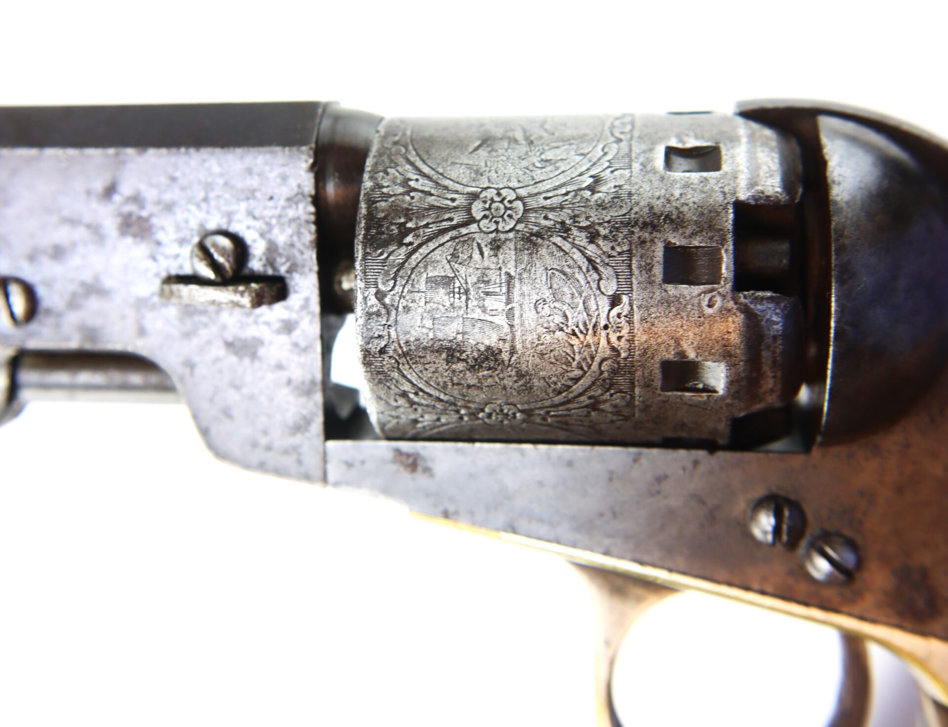Close-up of an antique revolver's cylinder, showing engraved decorative patterns on the metal surface.