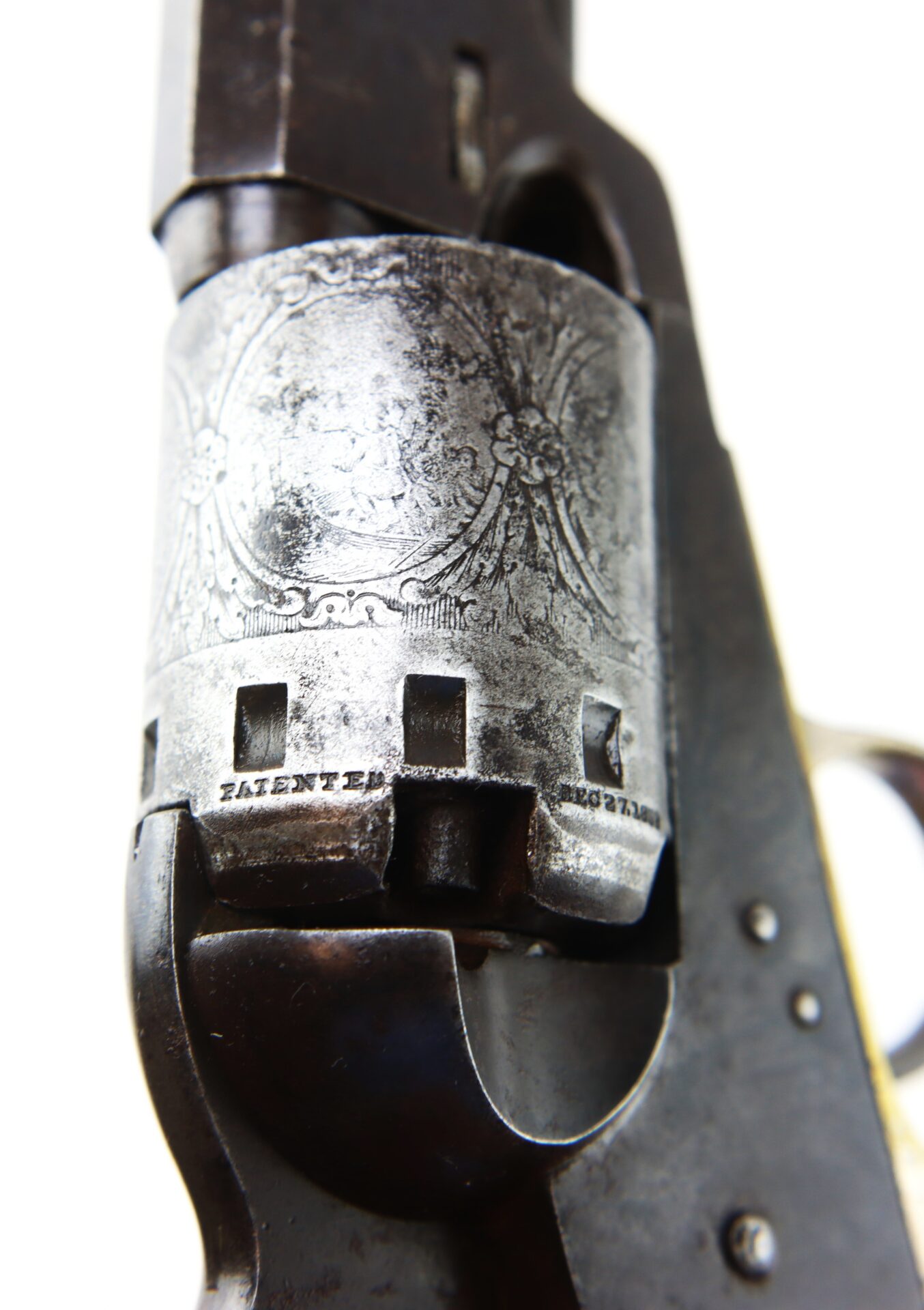 Close-up of the engraved cylinder of an antique revolver, showing metal texture and patent markings.