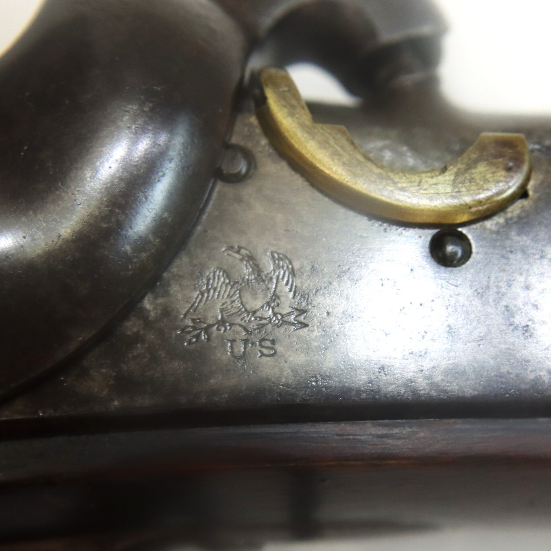 Close-up of a metal firearm with an engraved eagle, "U.S." inscription, and a brass trigger guard.