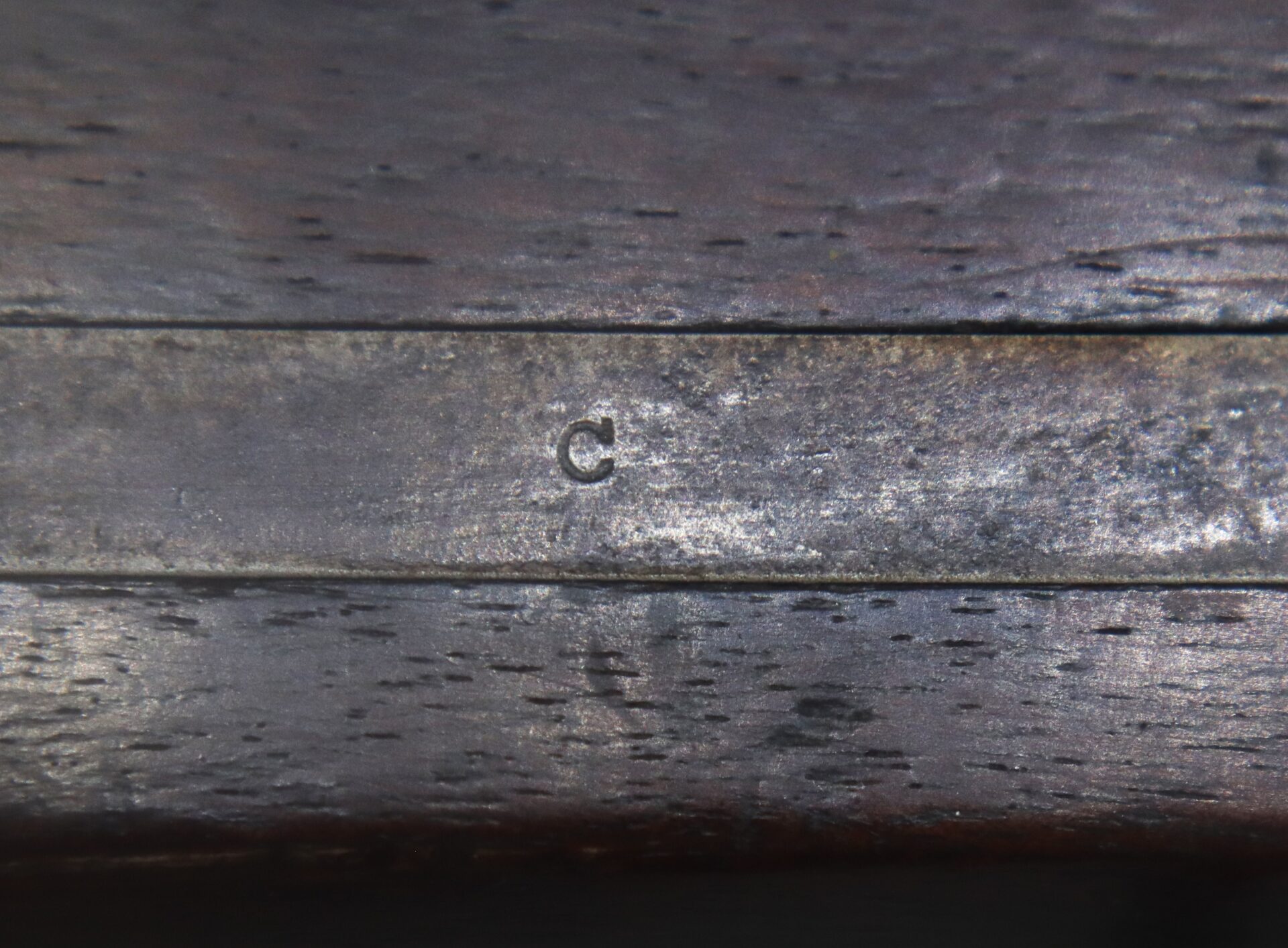 Close-up of a wooden and metal surface with the letter "C" engraved on the metal part.