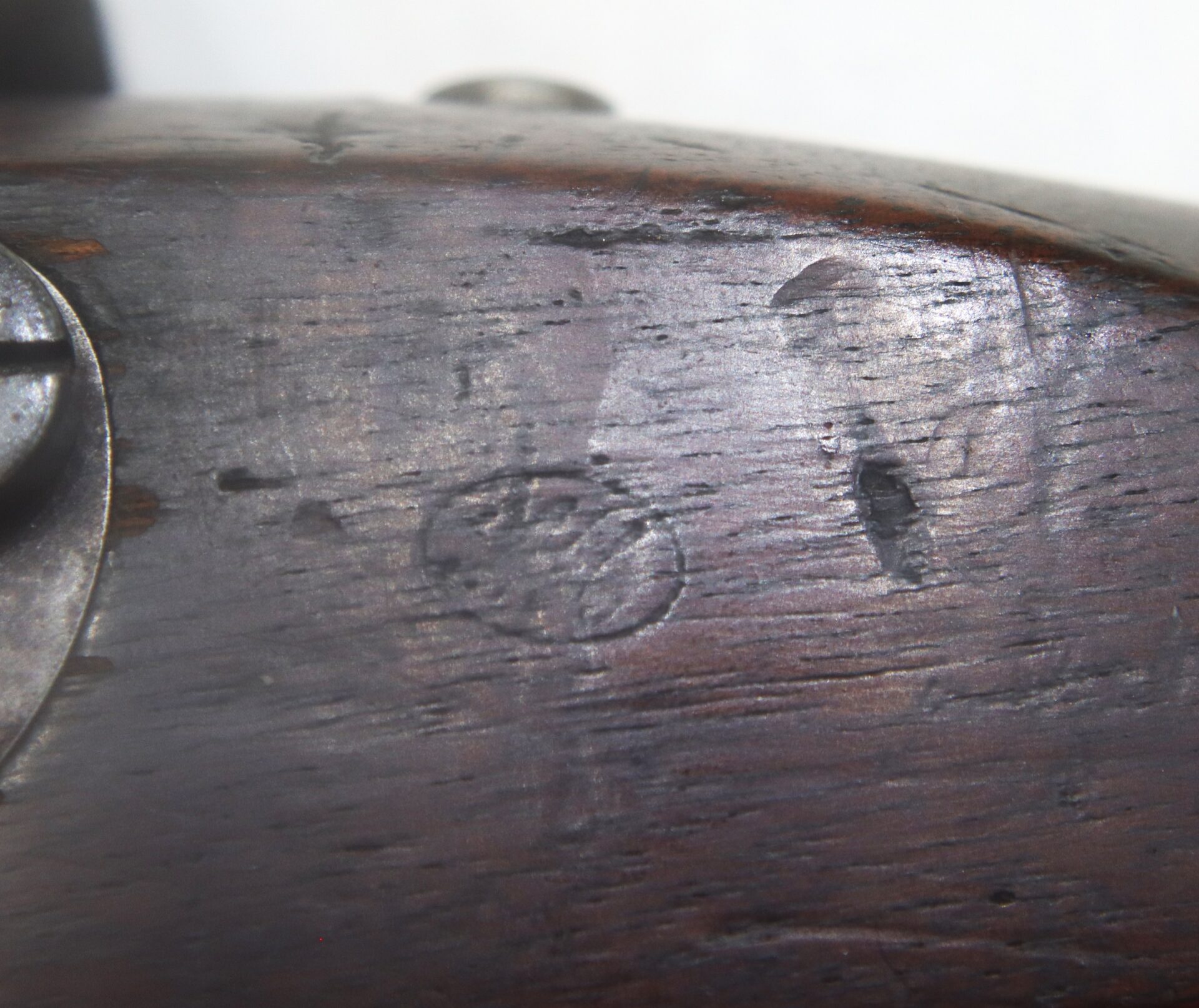 Close-up of a wooden rifle stock with visible wear, scratches, and a faint circular stamp or marking.