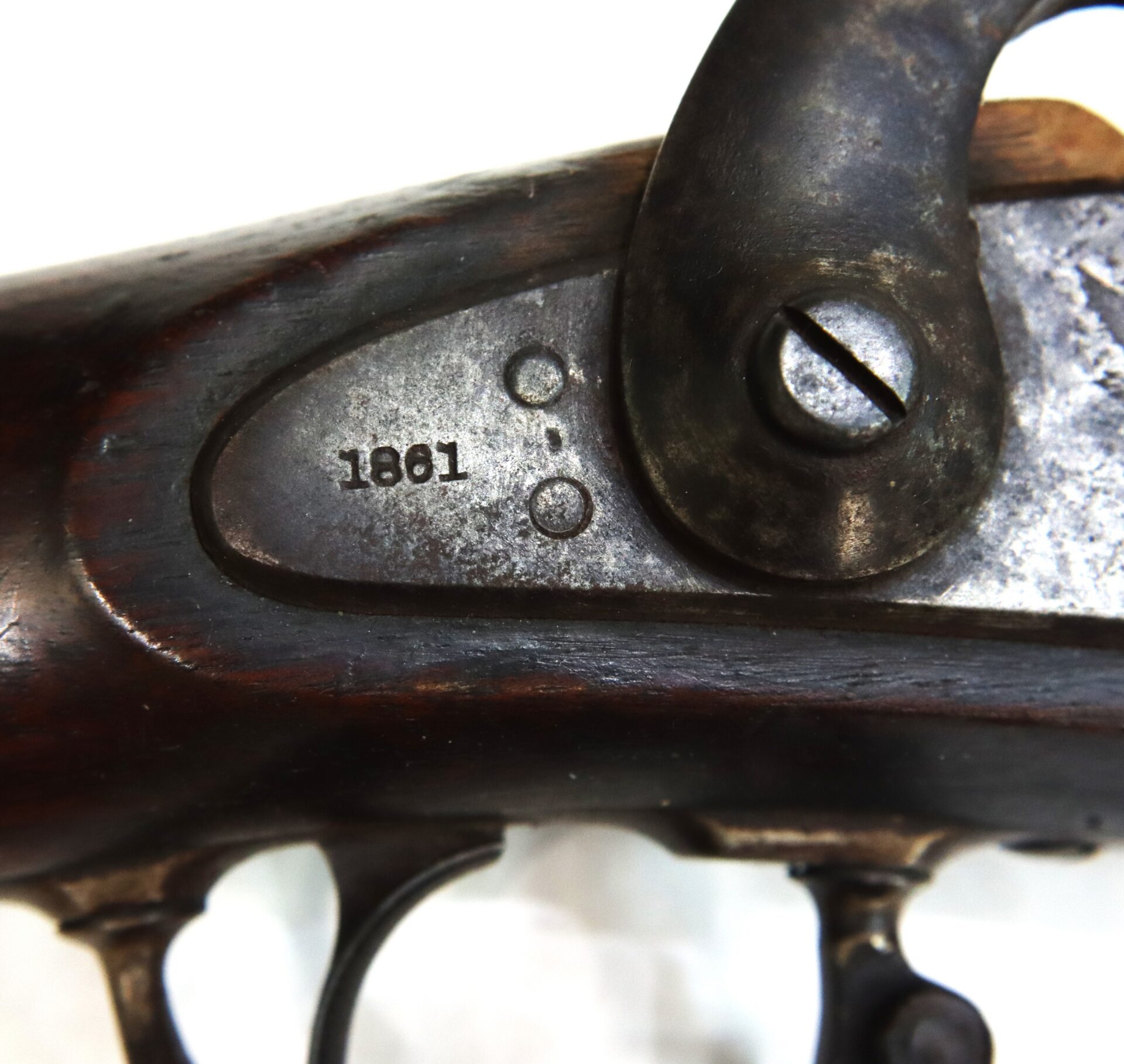 Close-up of an old rifle lock mechanism, showing a screw and the engraved year "1861" on the metal plate.