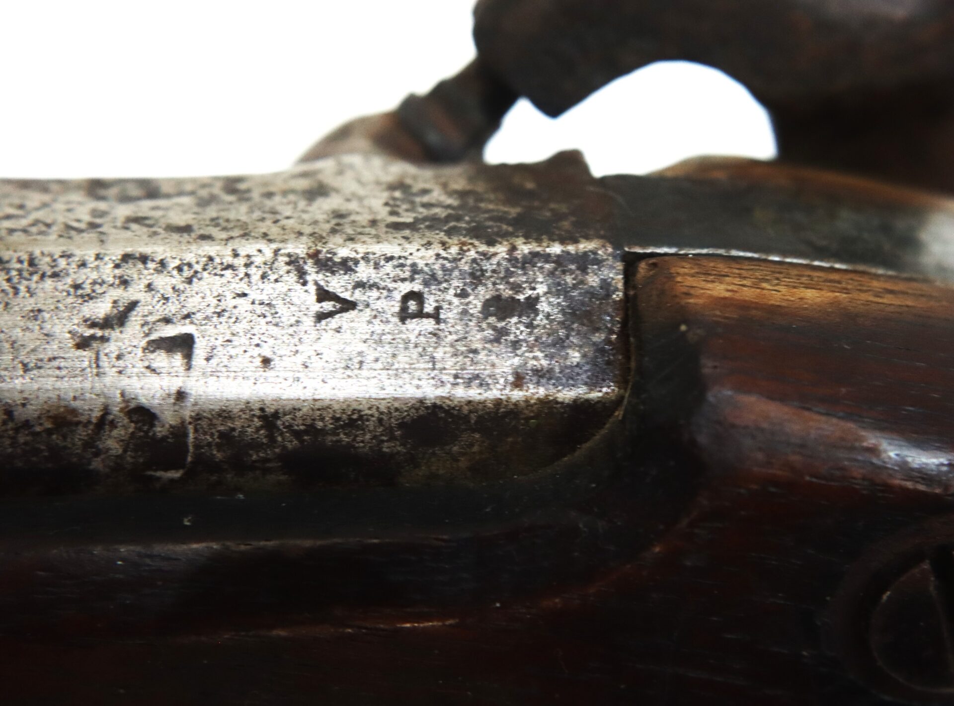 Close-up of a worn metal and wood surface on an antique firearm, showing partial markings and scratches.