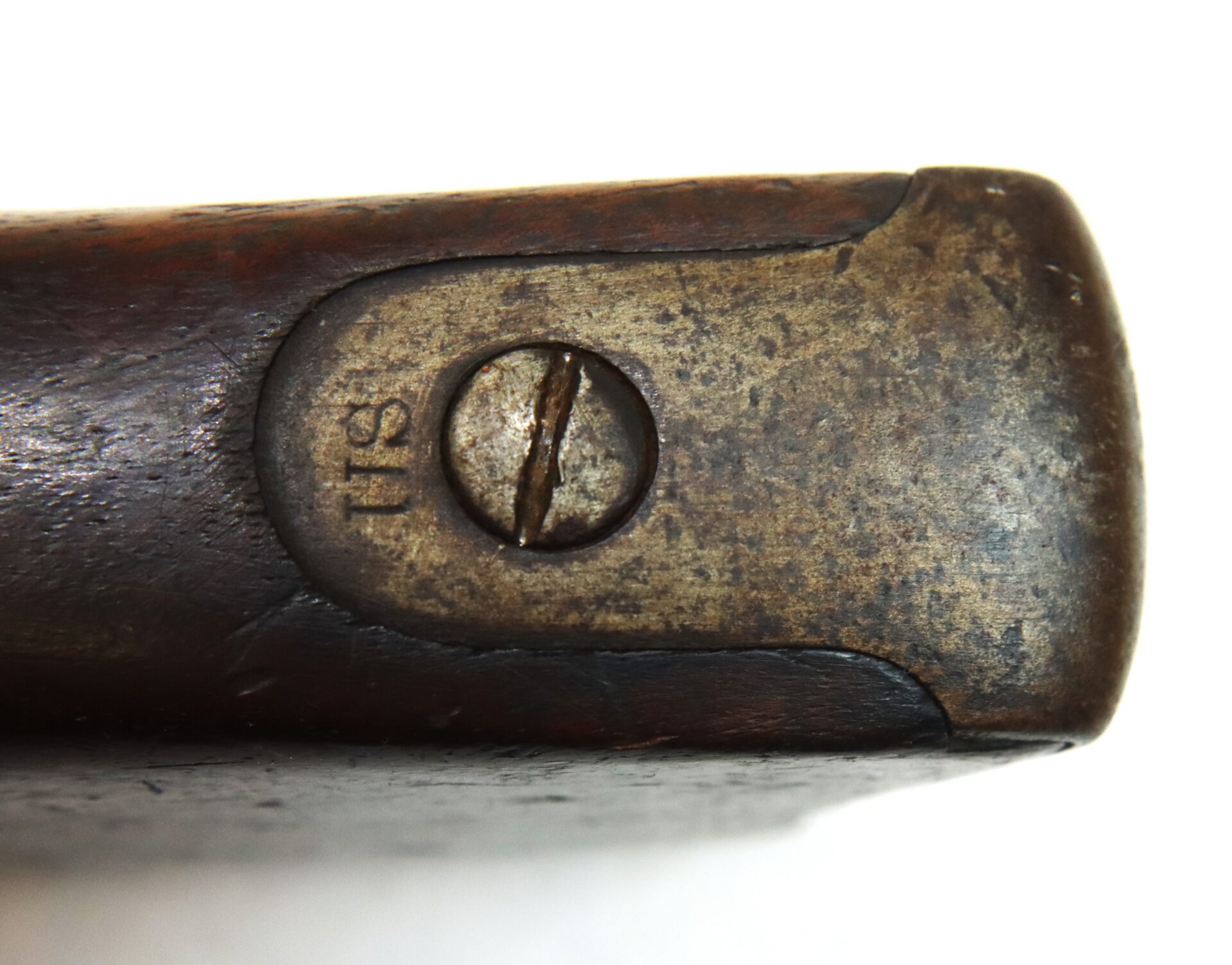 Close-up of a worn, metal buttplate on a wooden rifle stock, featuring a flat-head screw and the stamped number "511.