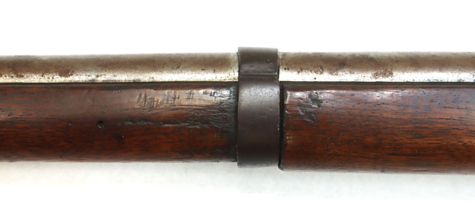 Close-up of an old rifle's wooden stock and metal barrel, showing a metal barrel band and signs of wear and aging on the surfaces.