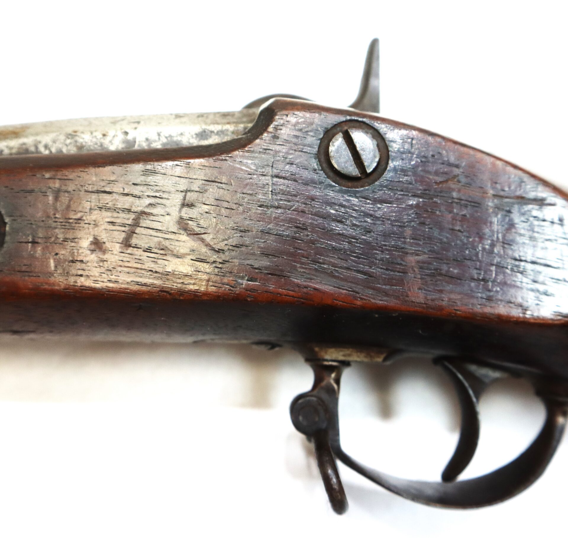 Close-up of an old wooden gun stock with a visible screw and trigger mechanism, showing worn and scratched wood surface.