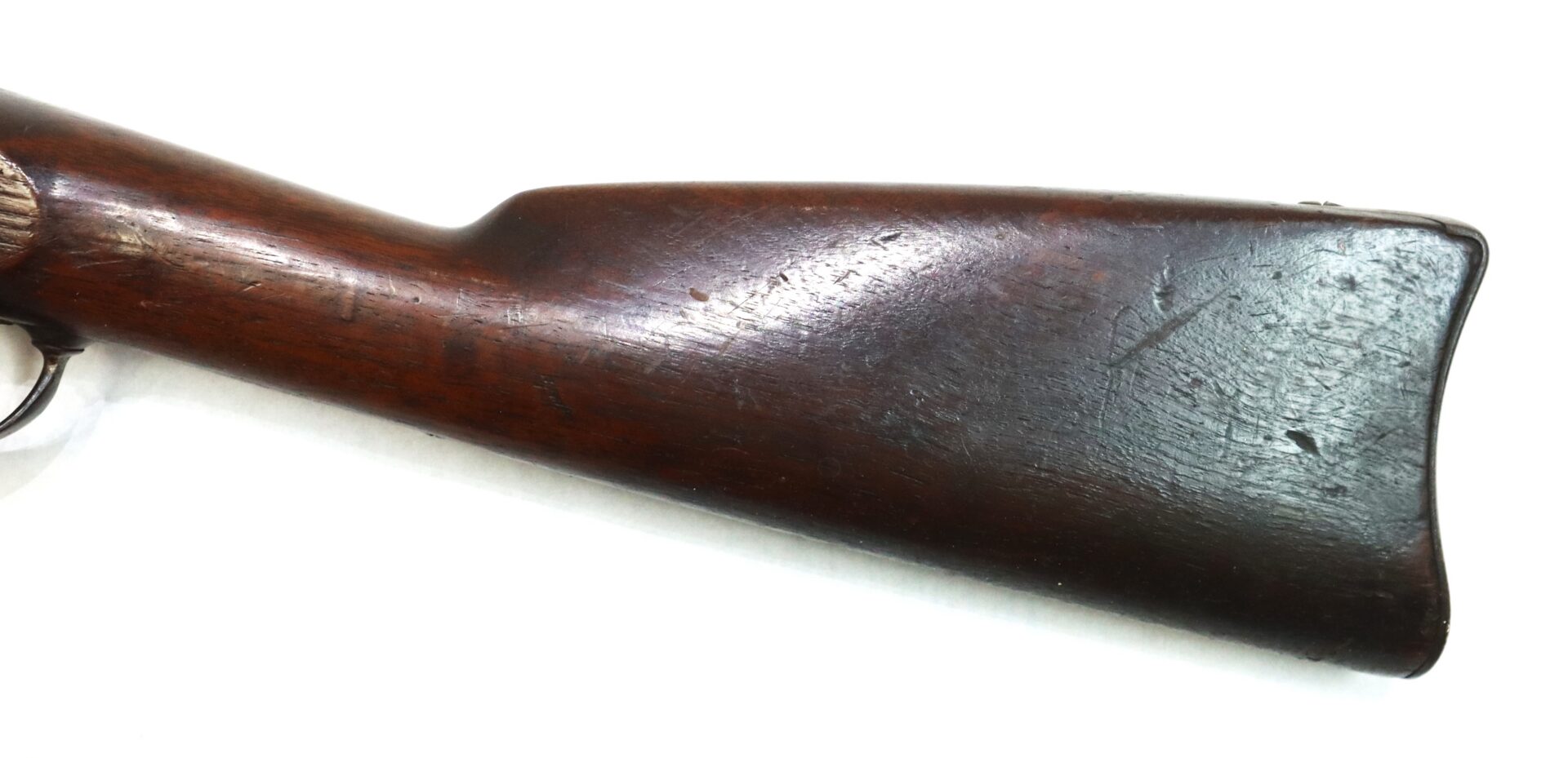 Close-up view of a wooden rifle stock, showing signs of wear and scratches, against a plain white background.