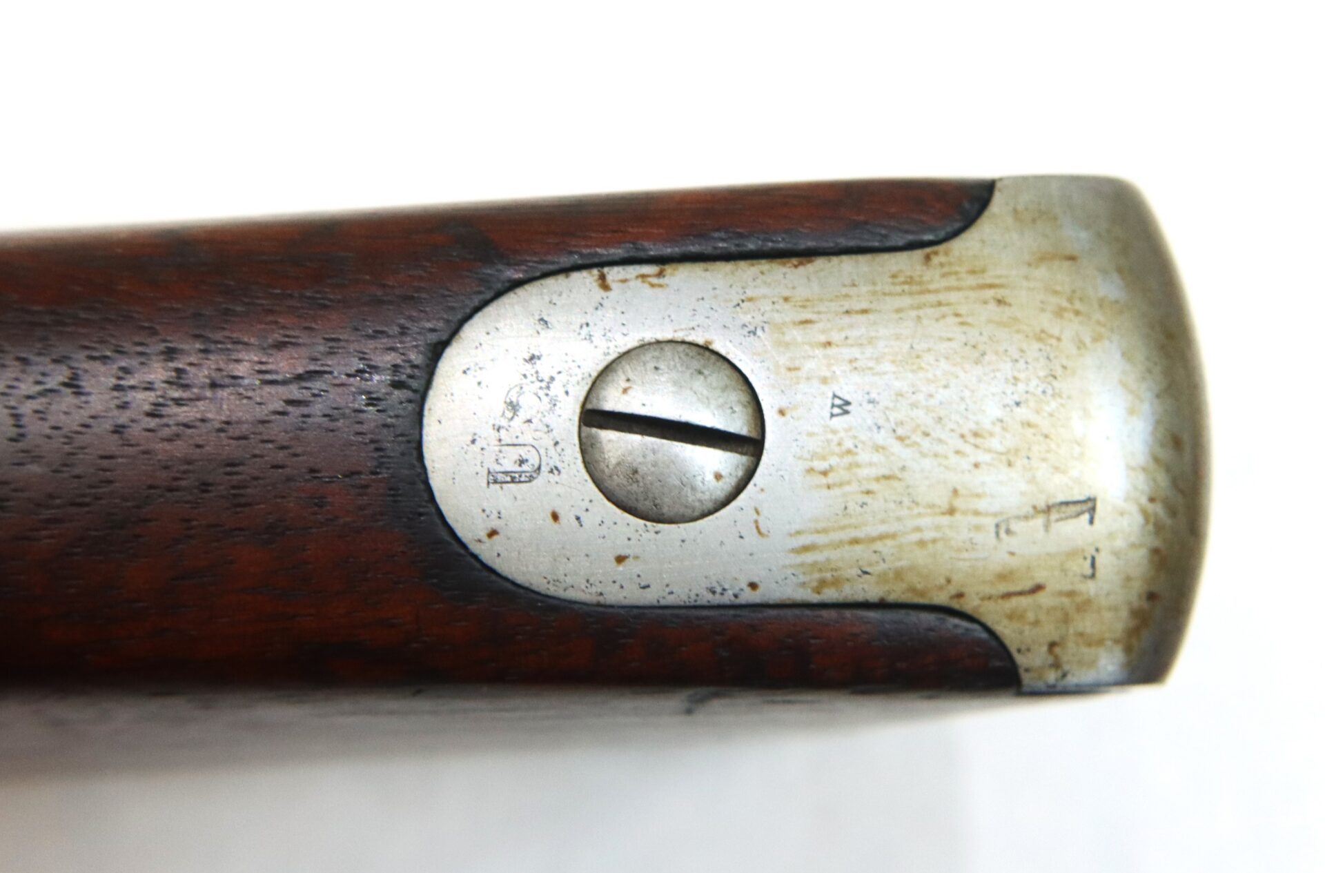 Close-up view of a metal buttplate with a flathead screw on the end of a wooden rifle stock, showing some wear and minor scratches.