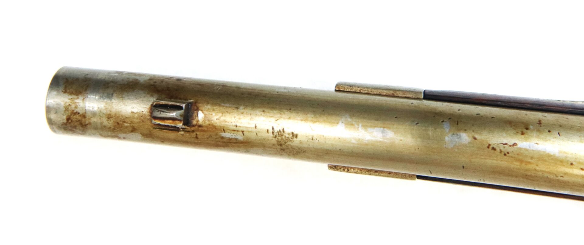 Close-up of an aged brass rifle barrel with a front sight and some visible tarnish and scratches.