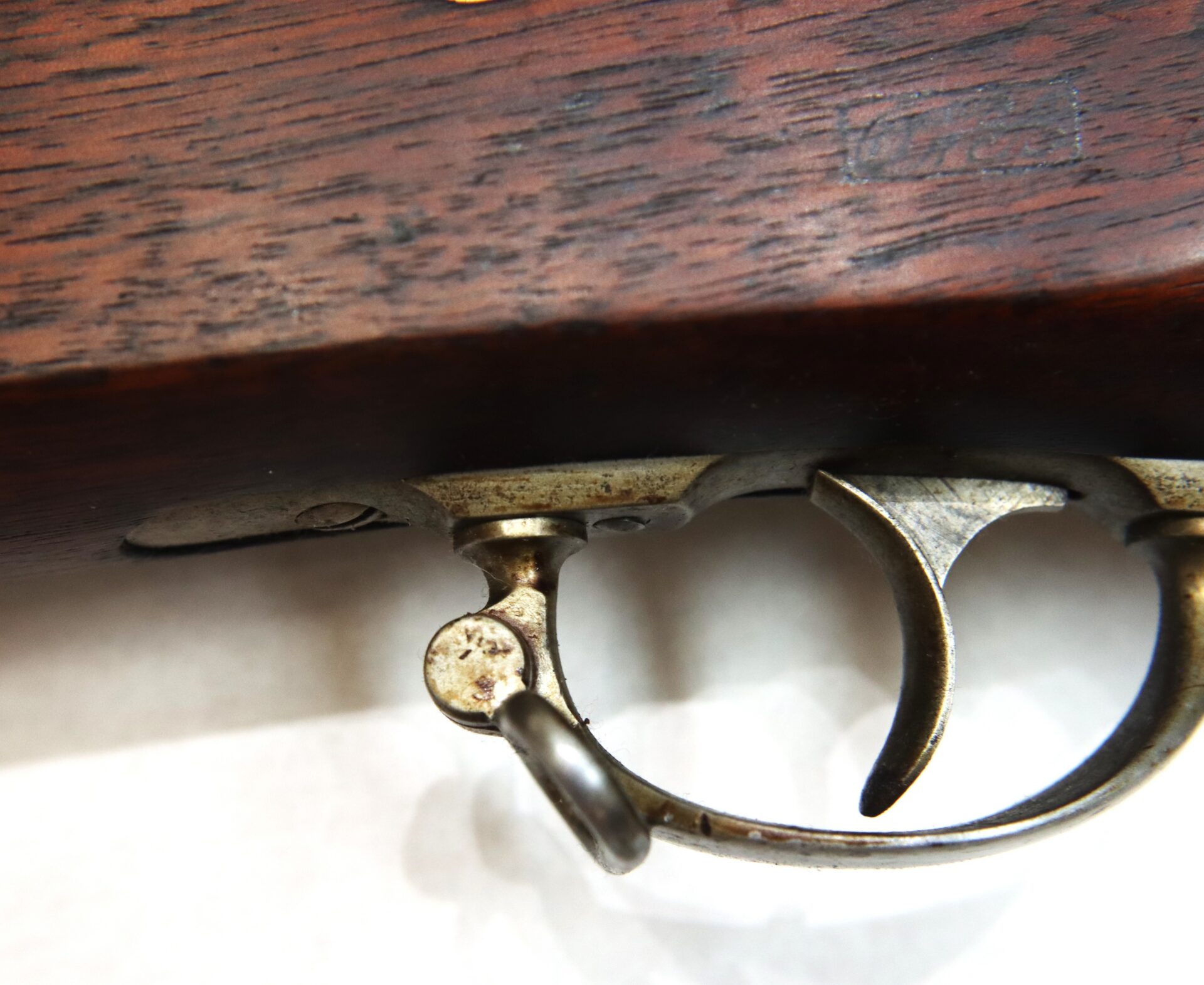 Close-up view of a metallic trigger and trigger guard on a wooden firearm stock.