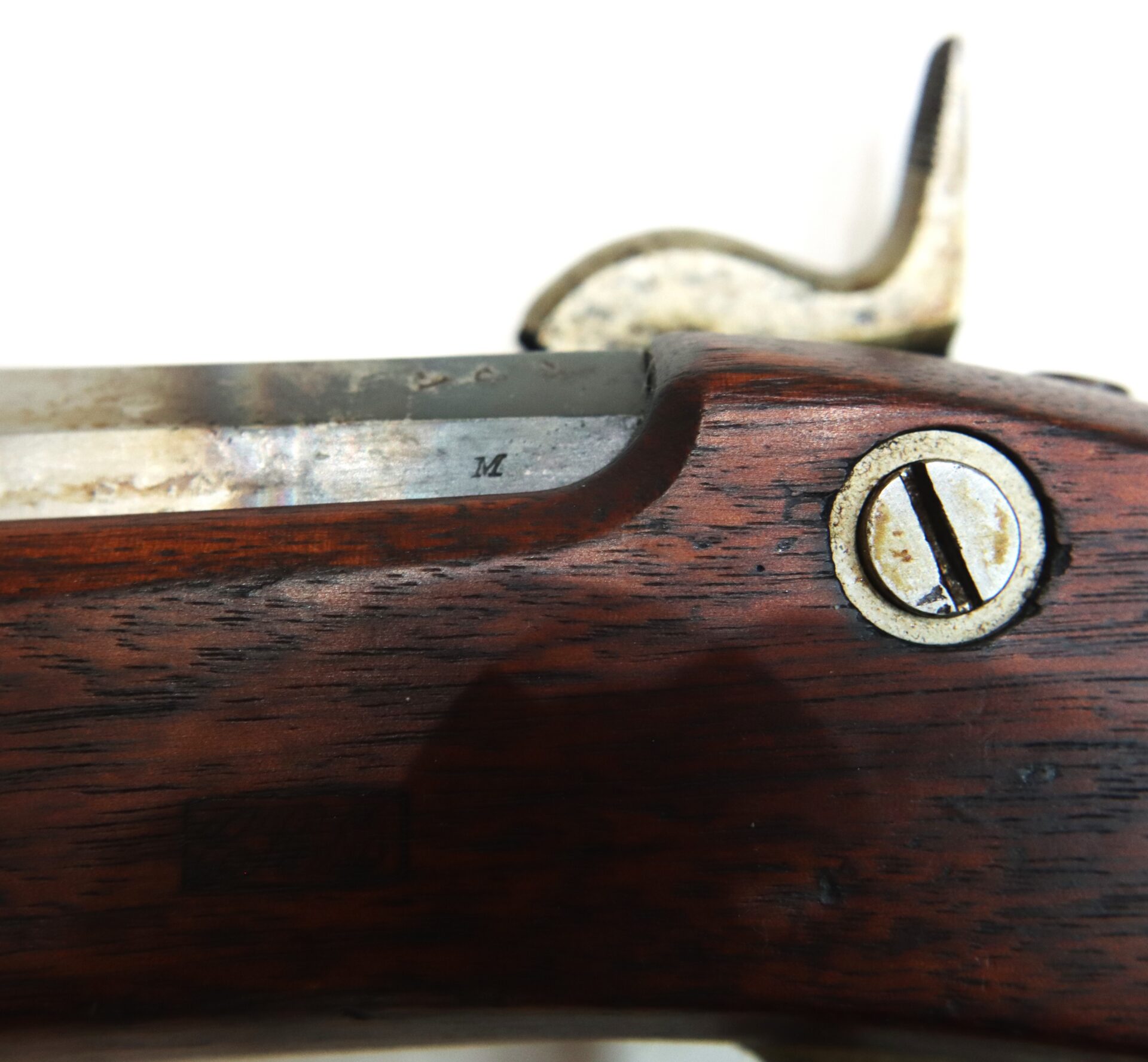 Close-up of a wooden rifle stock showing a metal screw, a stamped letter "M", and part of the gun's metal action.