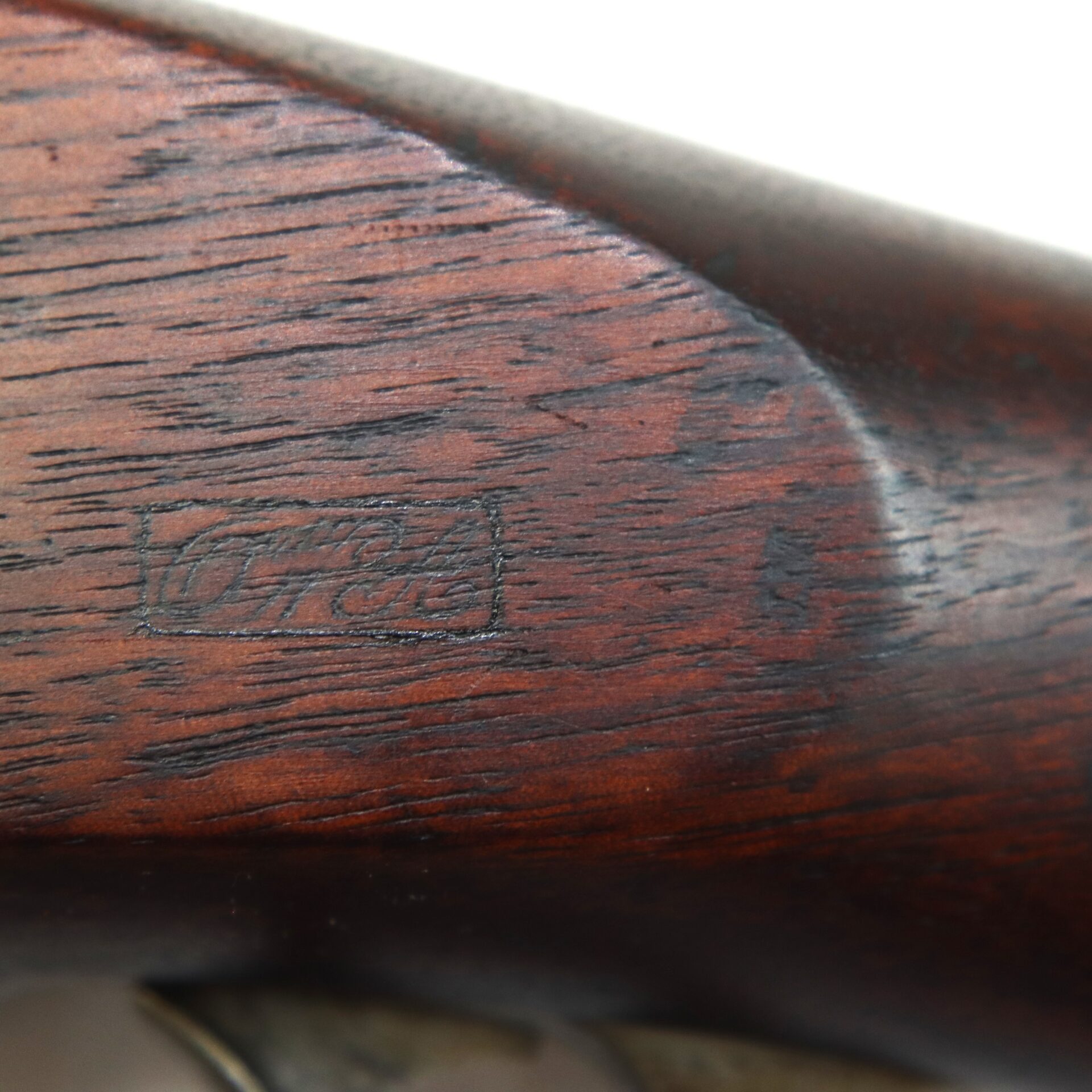Close-up of a wooden rifle stock featuring an engraved rectangular marking with faint, indistinct text.