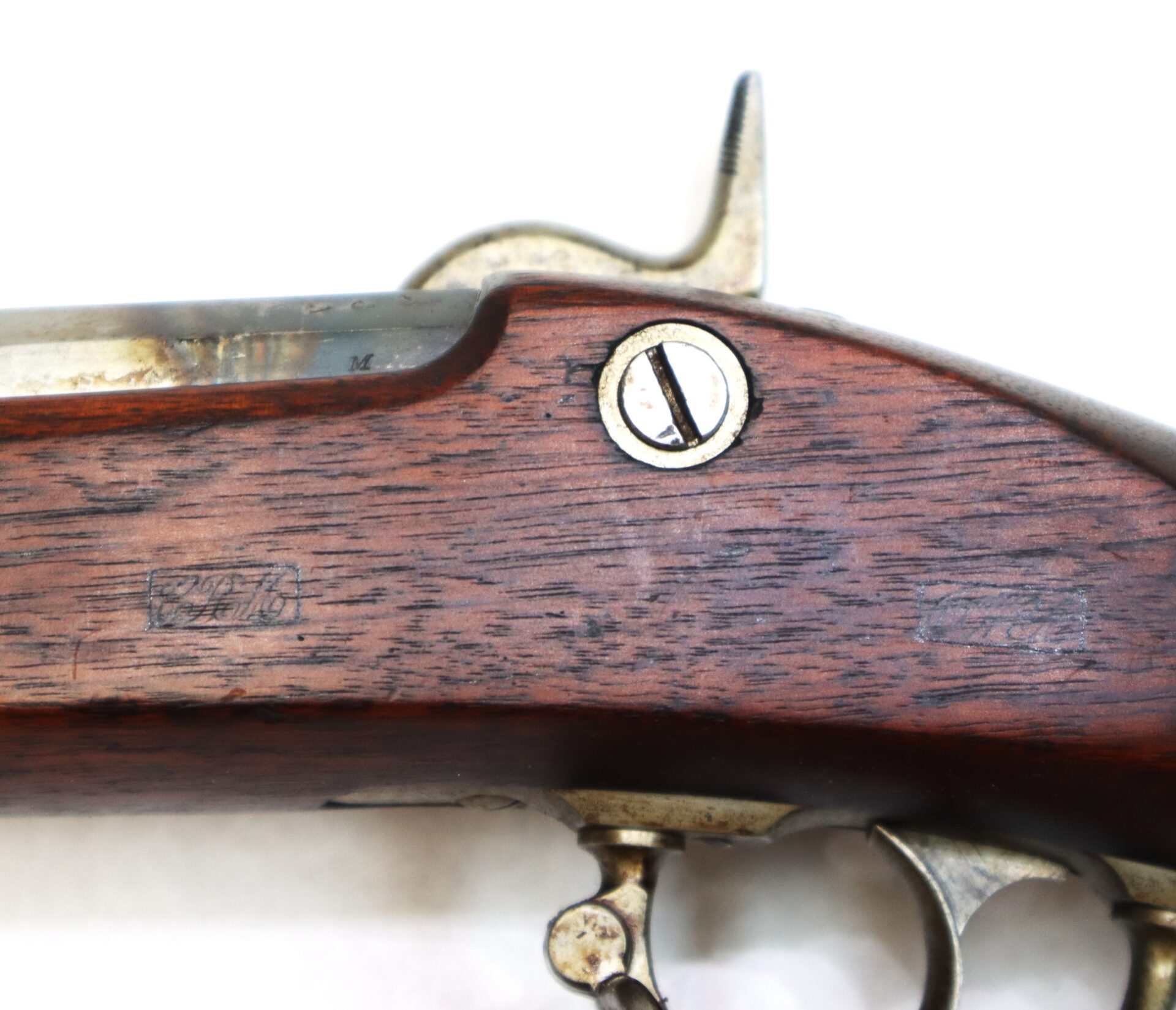 Close-up view of the wooden stock and metal mechanisms of a vintage firearm, showing a screw and some faint markings on the wood.