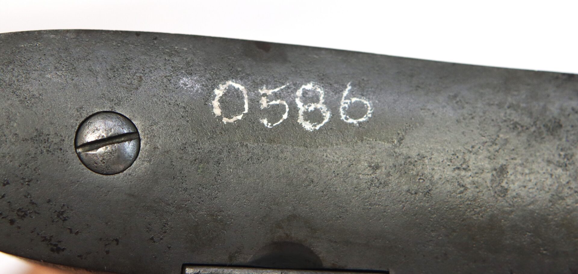 Close-up of a metal surface with a slotted screw and the number "0586" etched into it.
