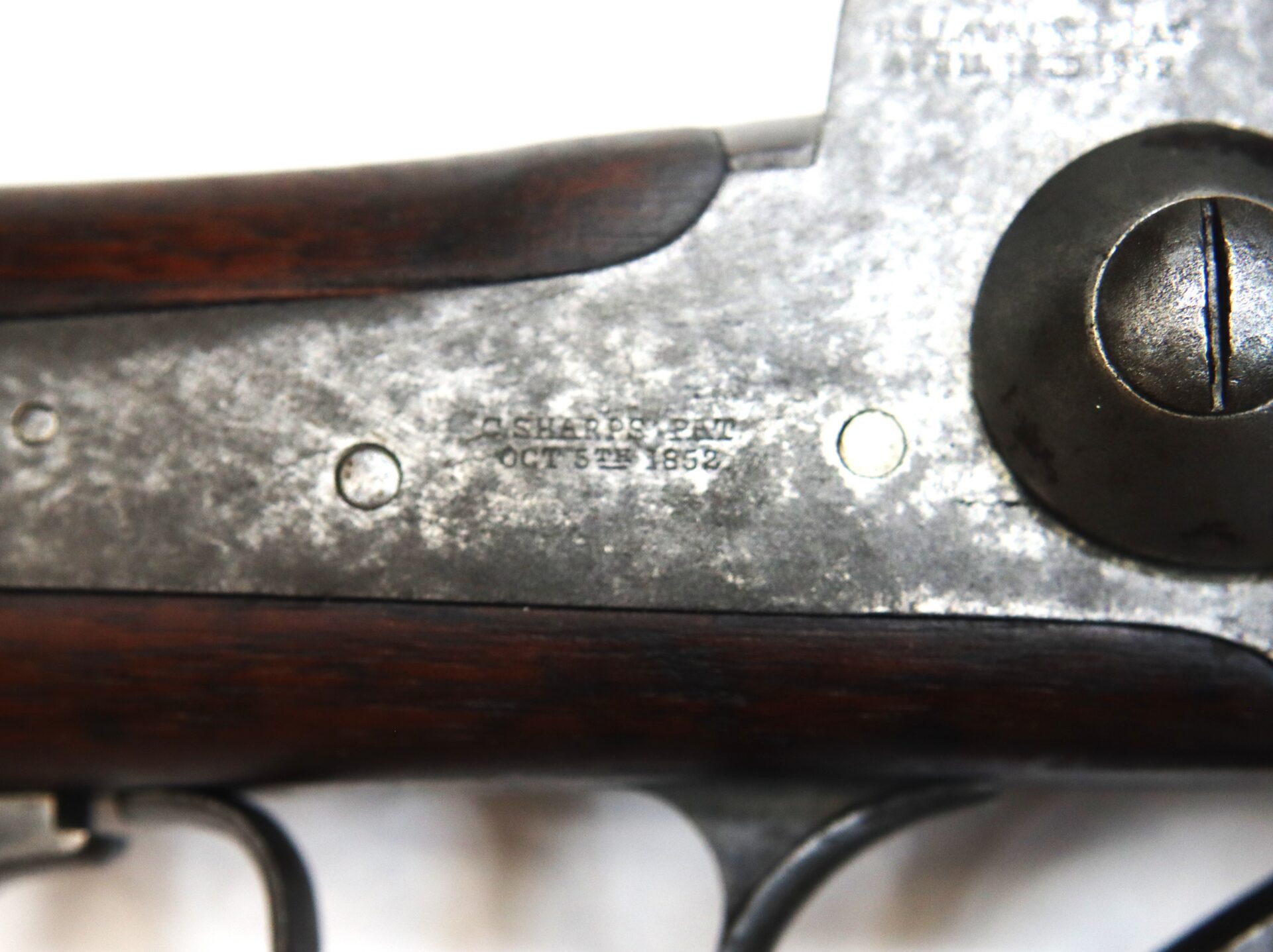 Close-up of a vintage firearm showing a metal plate engraved with "SHARPS PAT OCT 5TH 1852," with visible wood and trigger components.