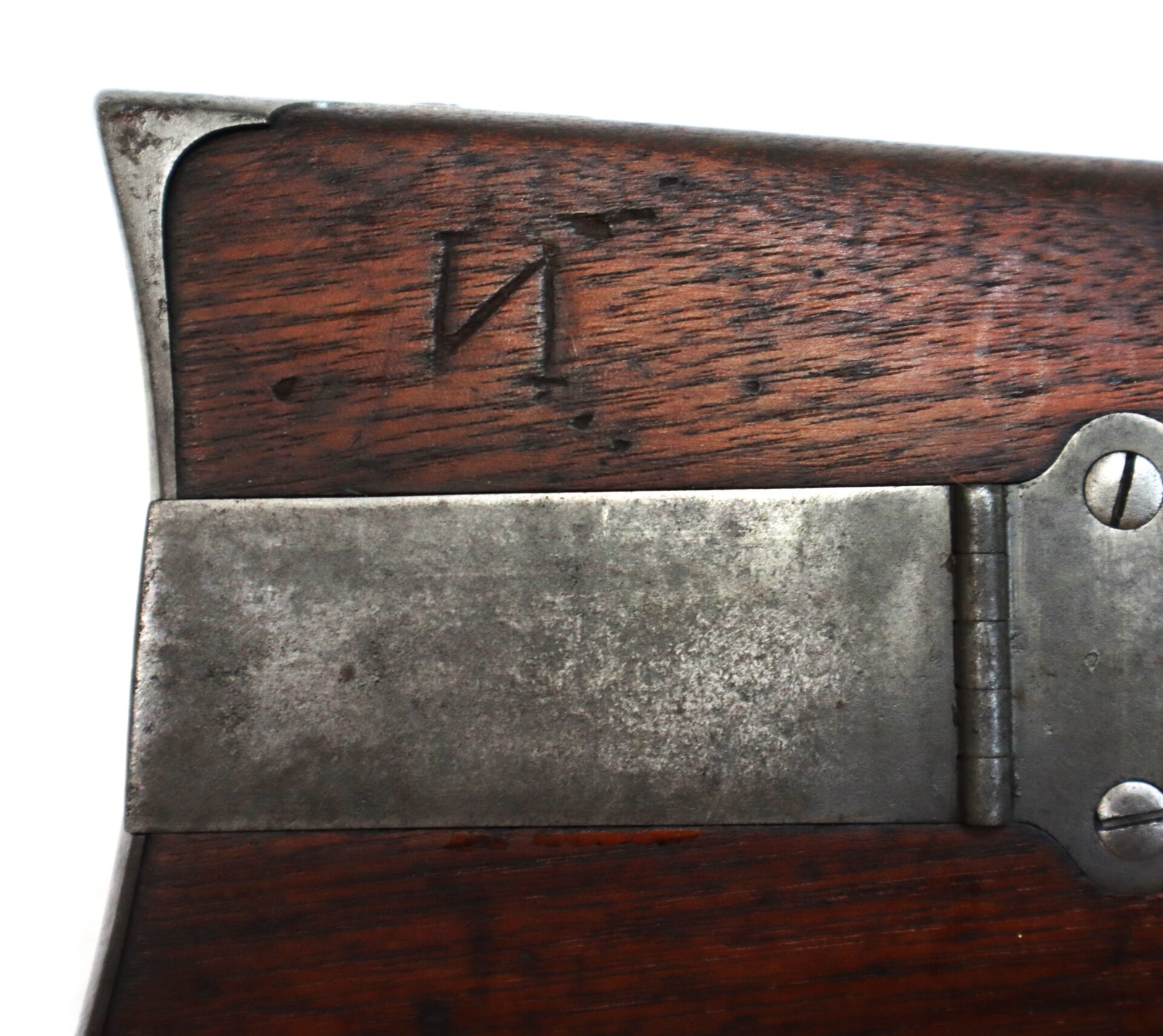 Close-up of a wooden rifle stock with a metal hinge and a Cyrillic letter "И" stamped into the wood.