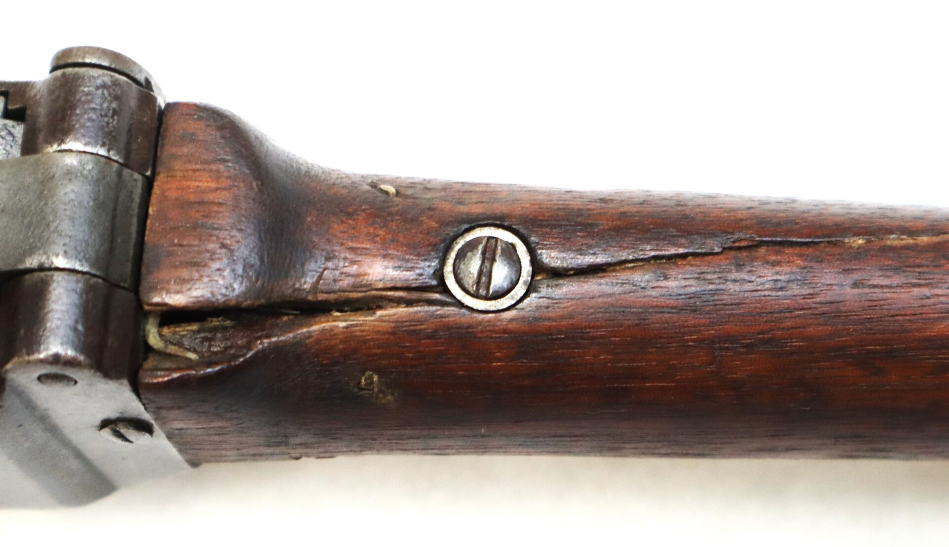 Close-up of a wooden rifle stock showing a large crack running through the wood, with a metal screw in the center.