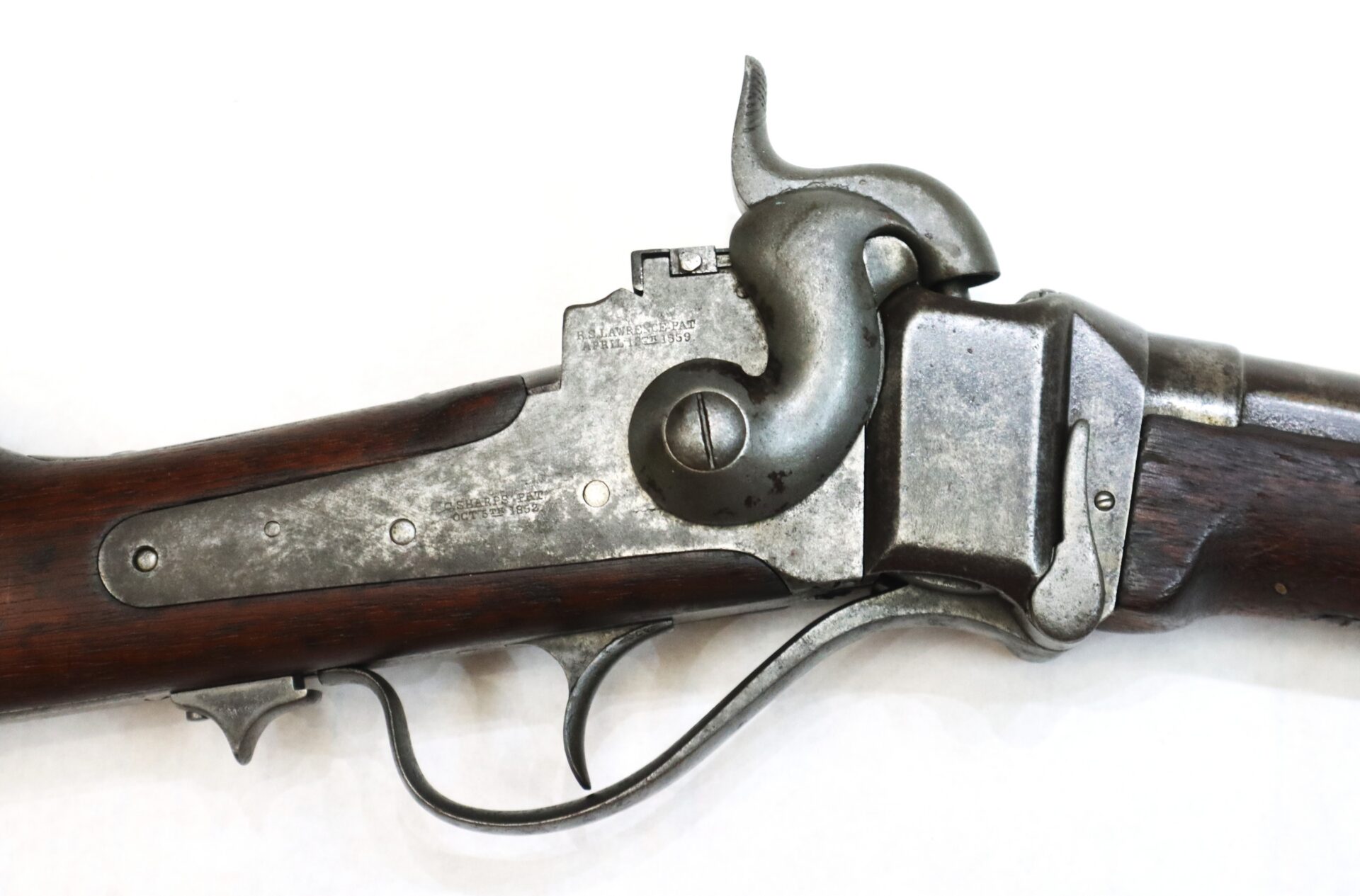 Close-up of an antique metal and wood lever-action rifle, showing the trigger, hammer, and part of the receiver against a white background.
