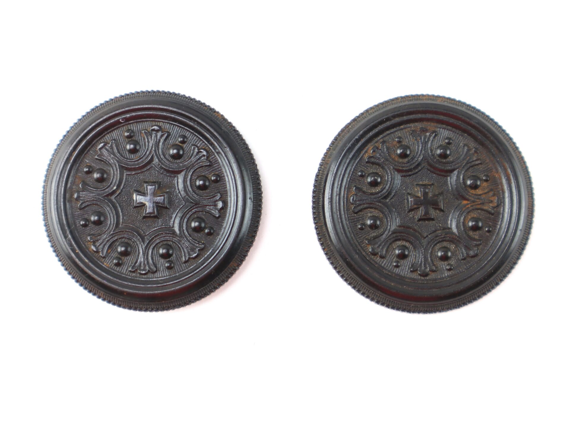 Two round, dark brown buttons with raised ornate patterns and a cross design in the center, displayed on a white background.