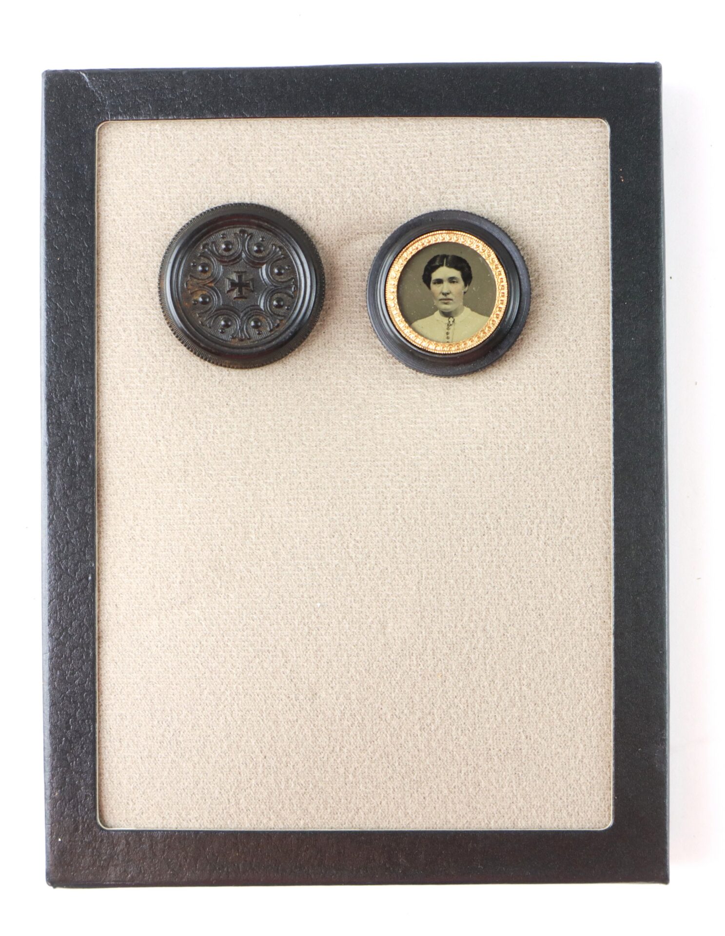 A small circular photograph of a woman and a decorative round black object are mounted side by side on a beige background within a black frame.